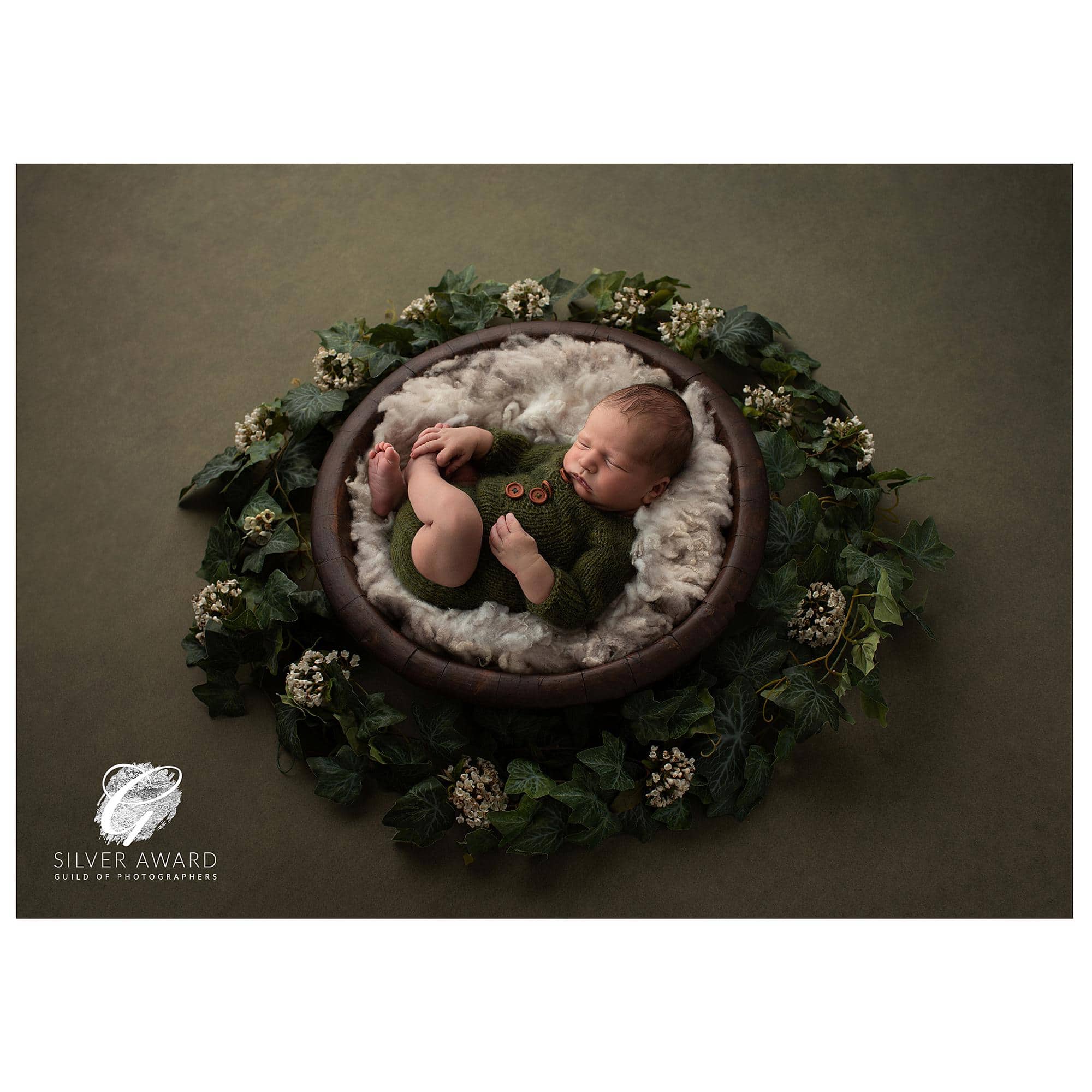 Photograph of a newborn baby in a wooden bowl on an olive backdrop wins a Silver Award at the Portrait Masters