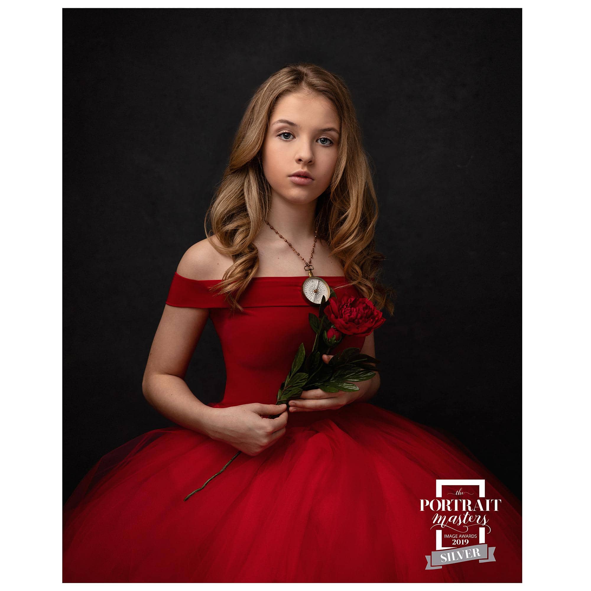 Portrait of a Girl in a red dress holding a red rose wins a silver award at the Portrait Masters
