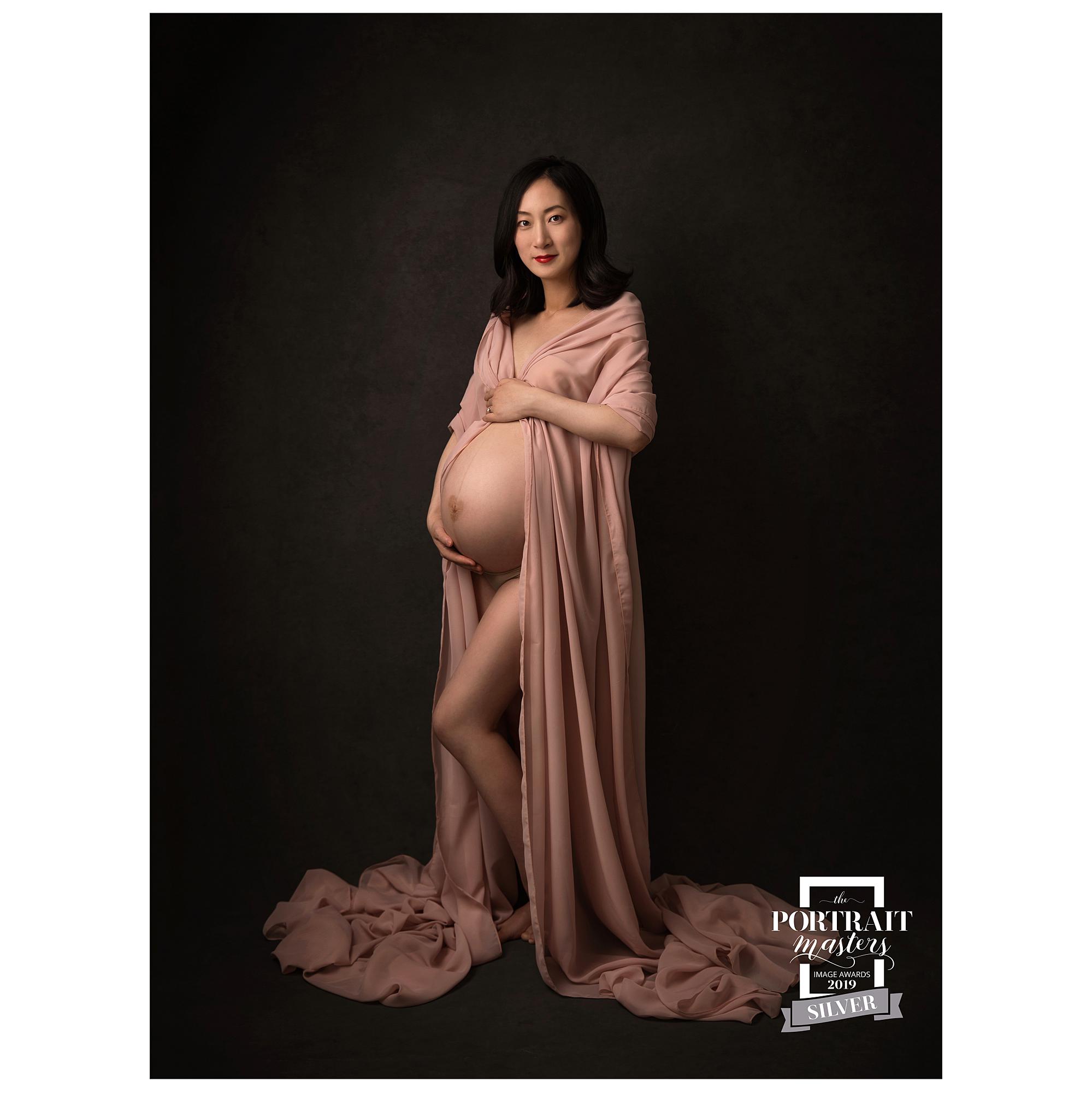 Pregnant woman posing in sheer pink material for a maternity photoshoot in Alison McKenny's Suffolk studio