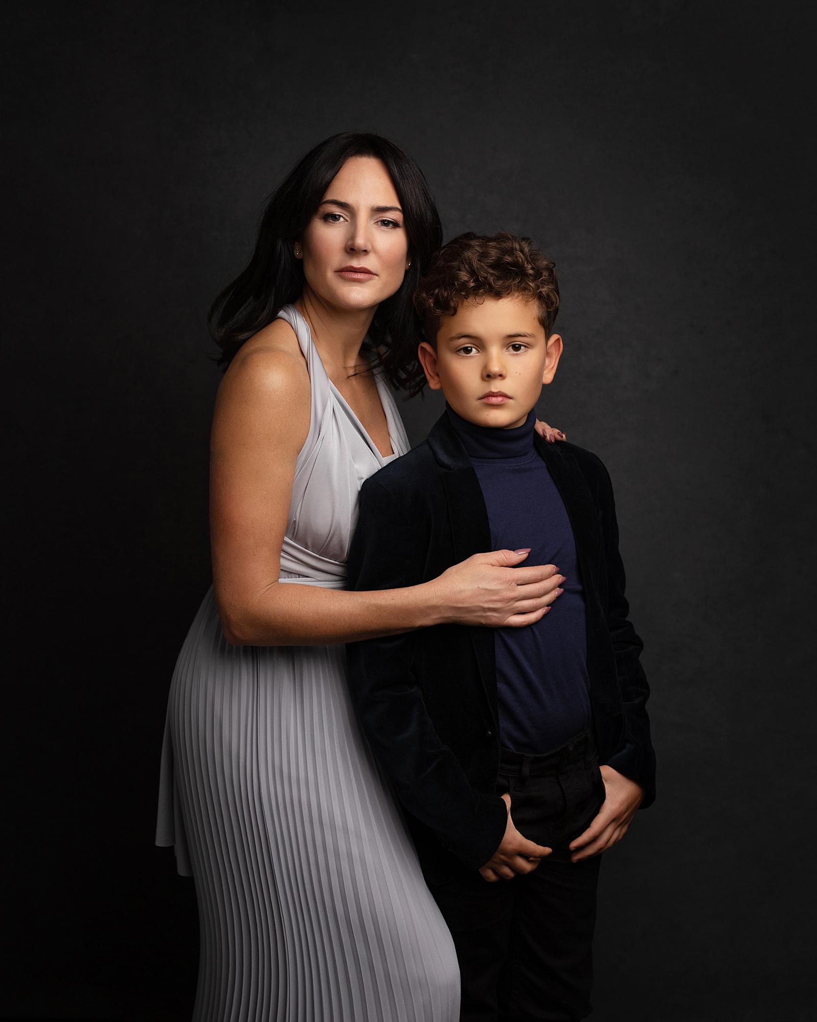 Black haired woman in a grey dress poses with her 9 year old son for a Beauty Shoot Photoshoot in a Suffolk studio