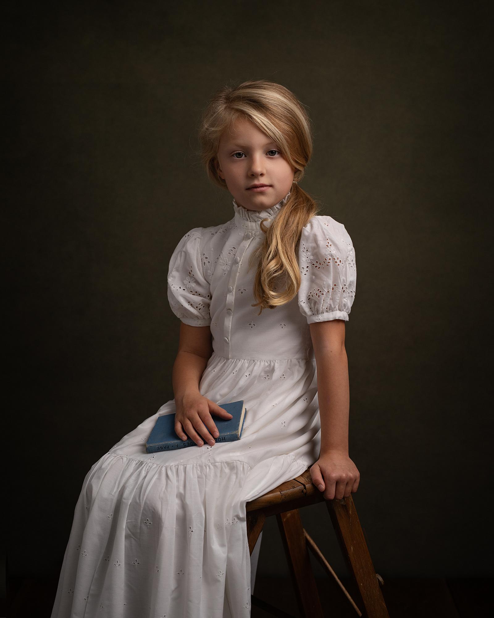 Little girl holds a book while wearing a vintage white dress in a Fine Art Photoshoot in Suffolk