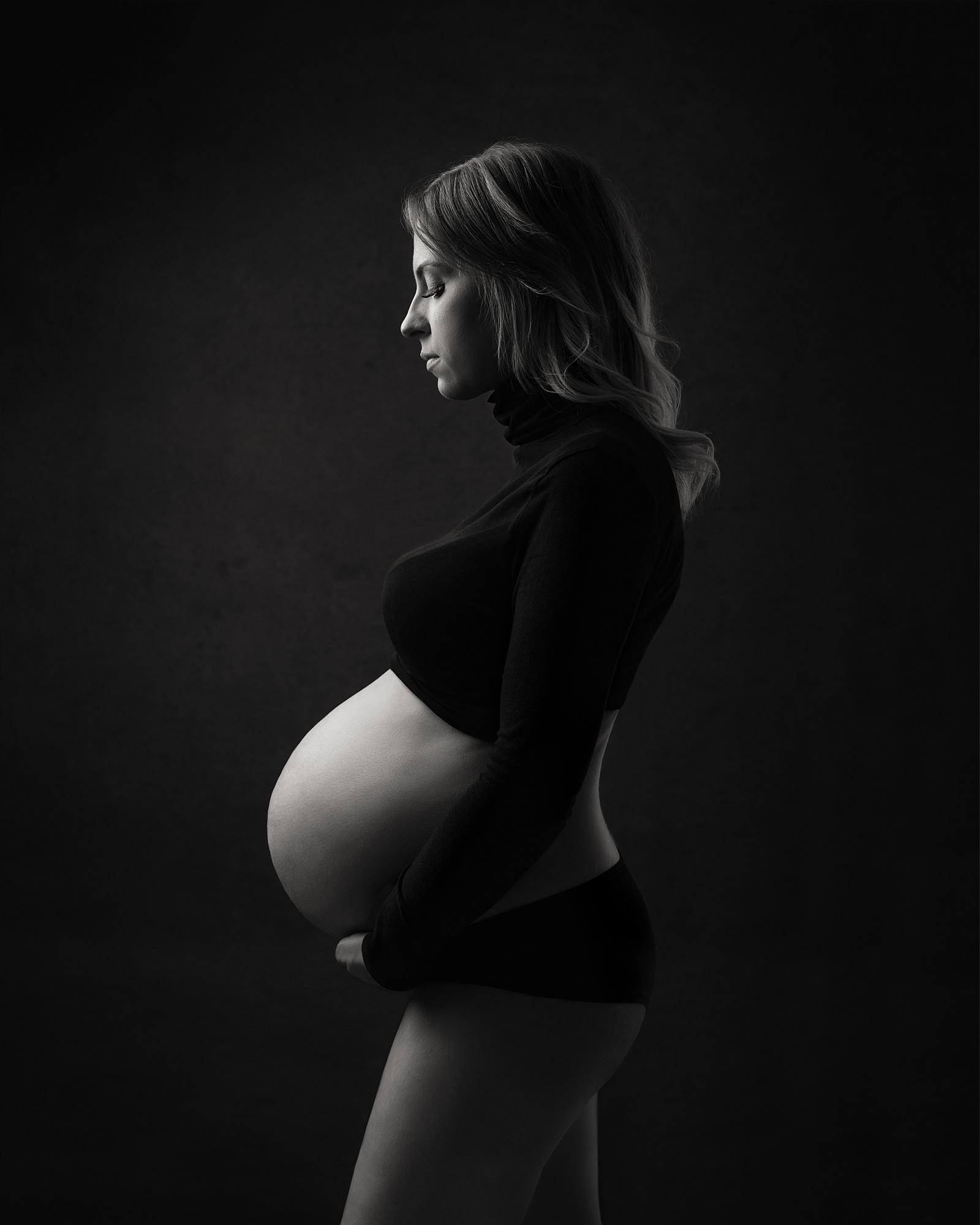 Black and white photograph of a pregnant womans profile against a black background