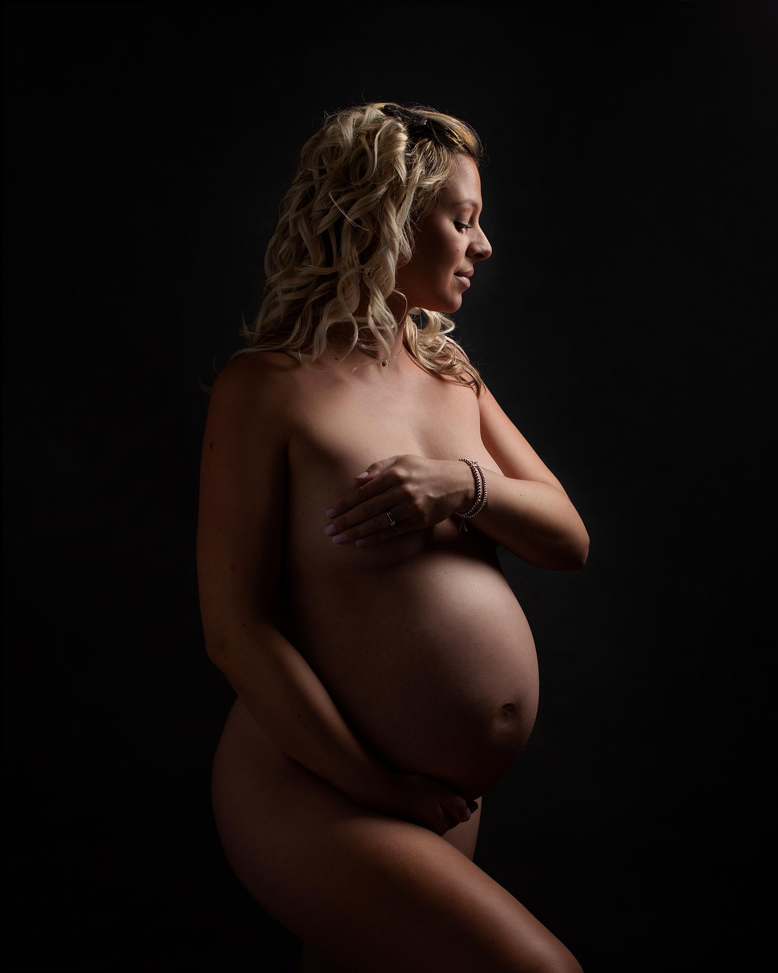 Pregnant woman posing against a black backdrop for a maternity photoshoot in Suffolk photography studio