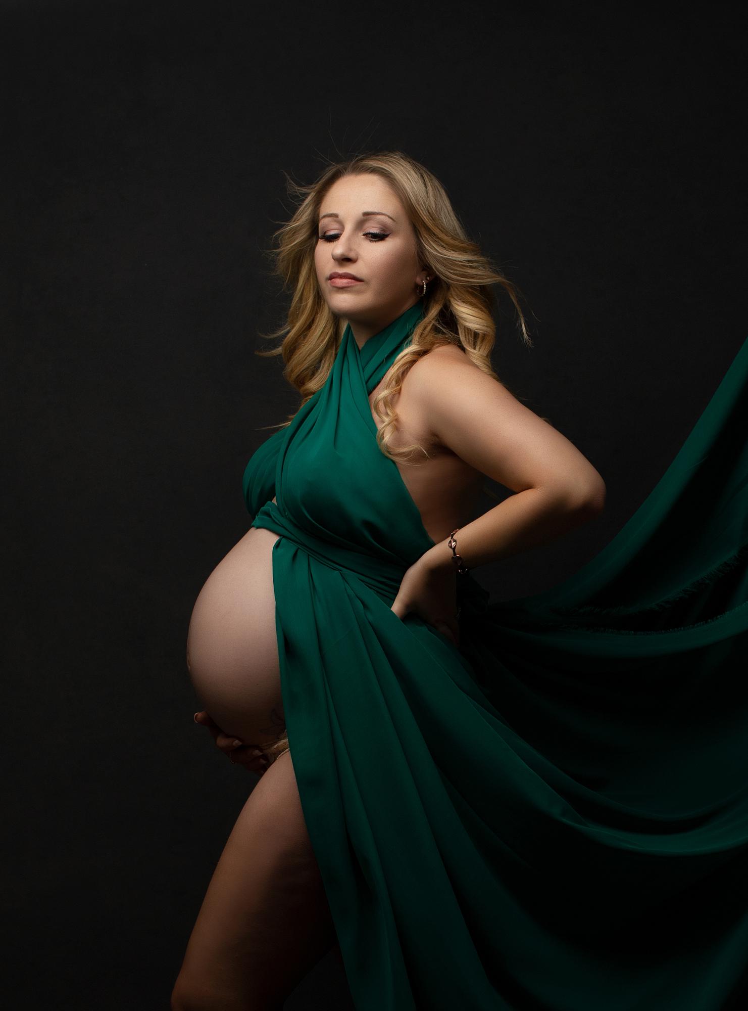 Pregnant woman posing against a black backdrop with flowing green material for a maternity photoshoot in Suffolk photography studio