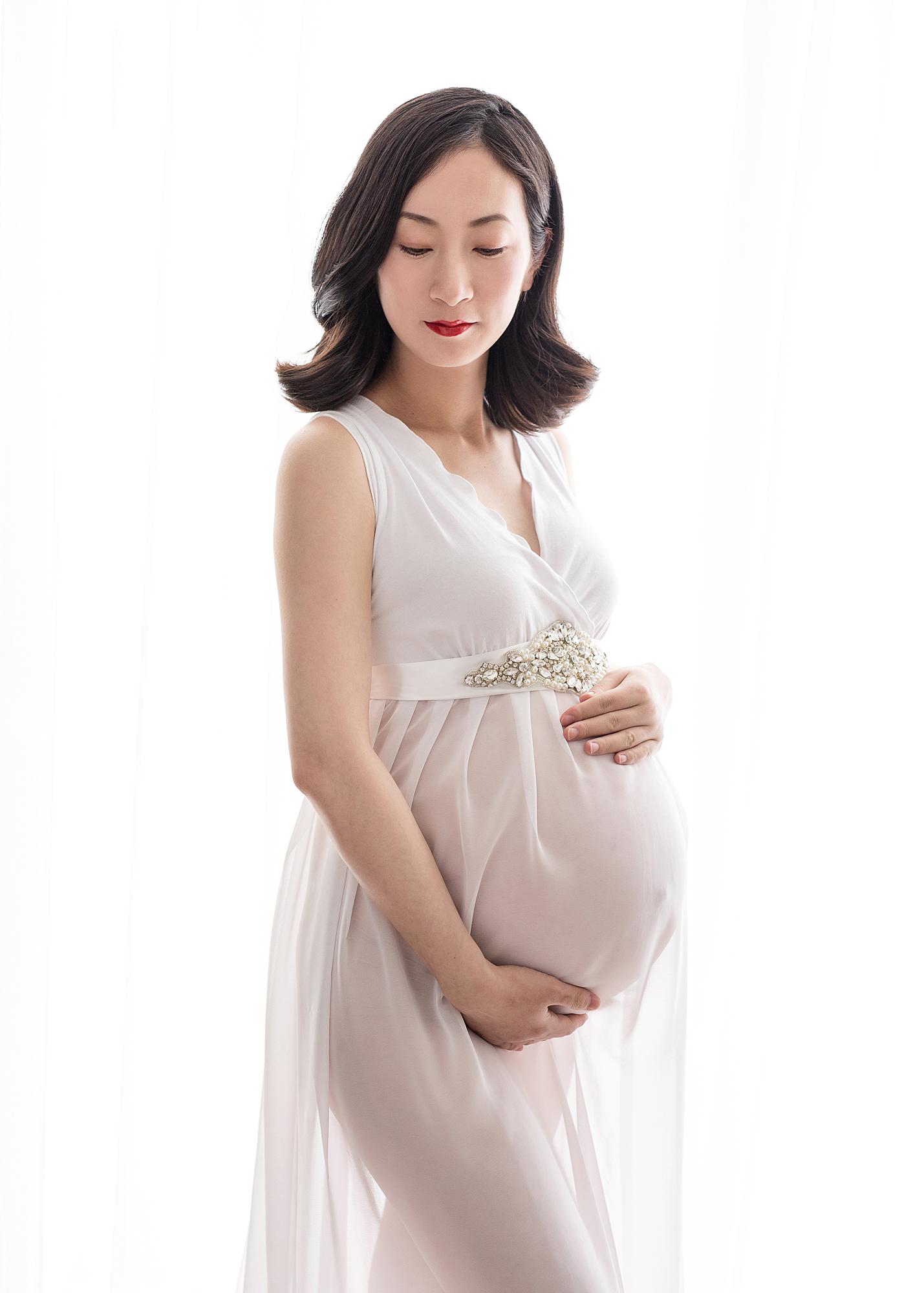 Pregnant woman posing in sheer white dress for a maternity photoshoot in Suffolk