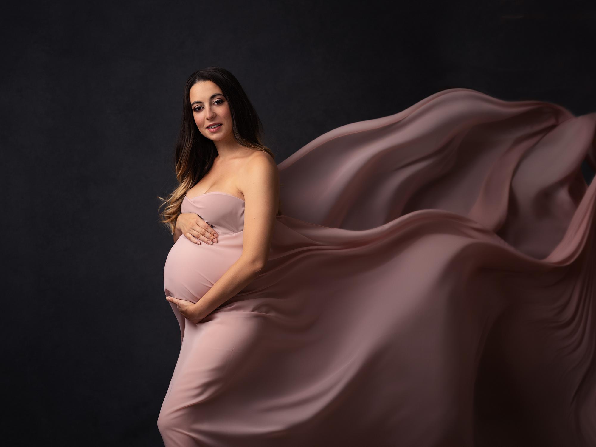 Pregnant woman poses while pink sheer material blows behind her