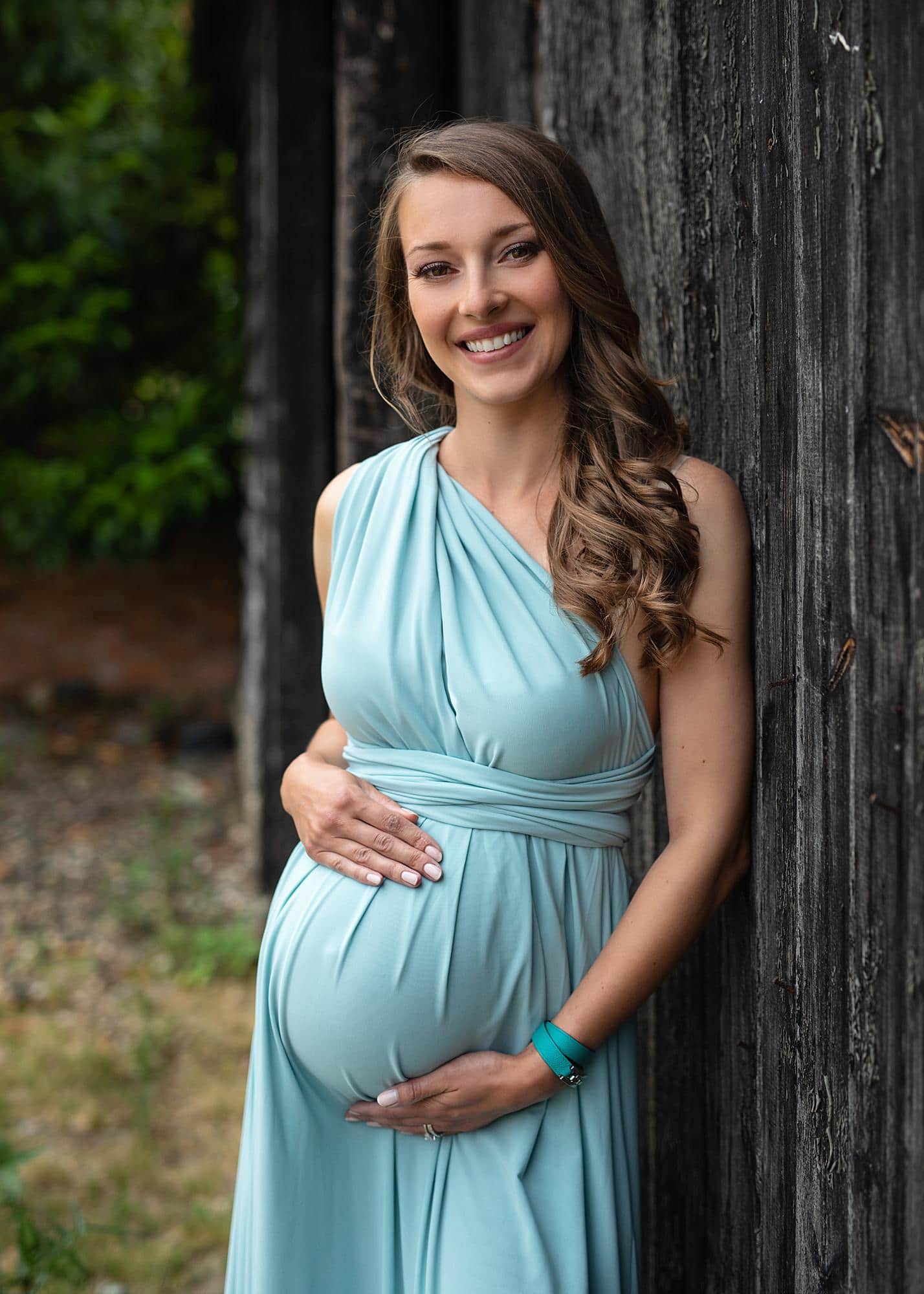 Pregnant woman posing in a blue dress against a barn door for a maternity photography shoot in Suffolk