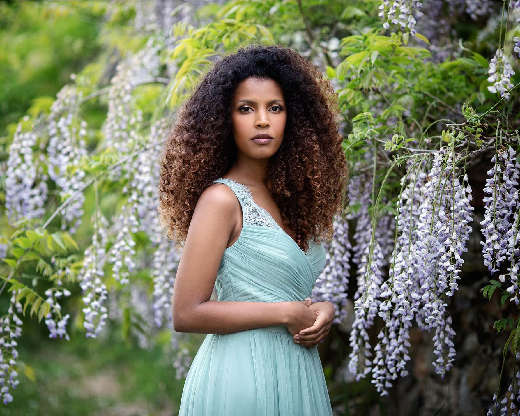 Beautiful woman stands by a wisteria bush wearing a green dress for an outdoor beauty photoshoot in Suffolk