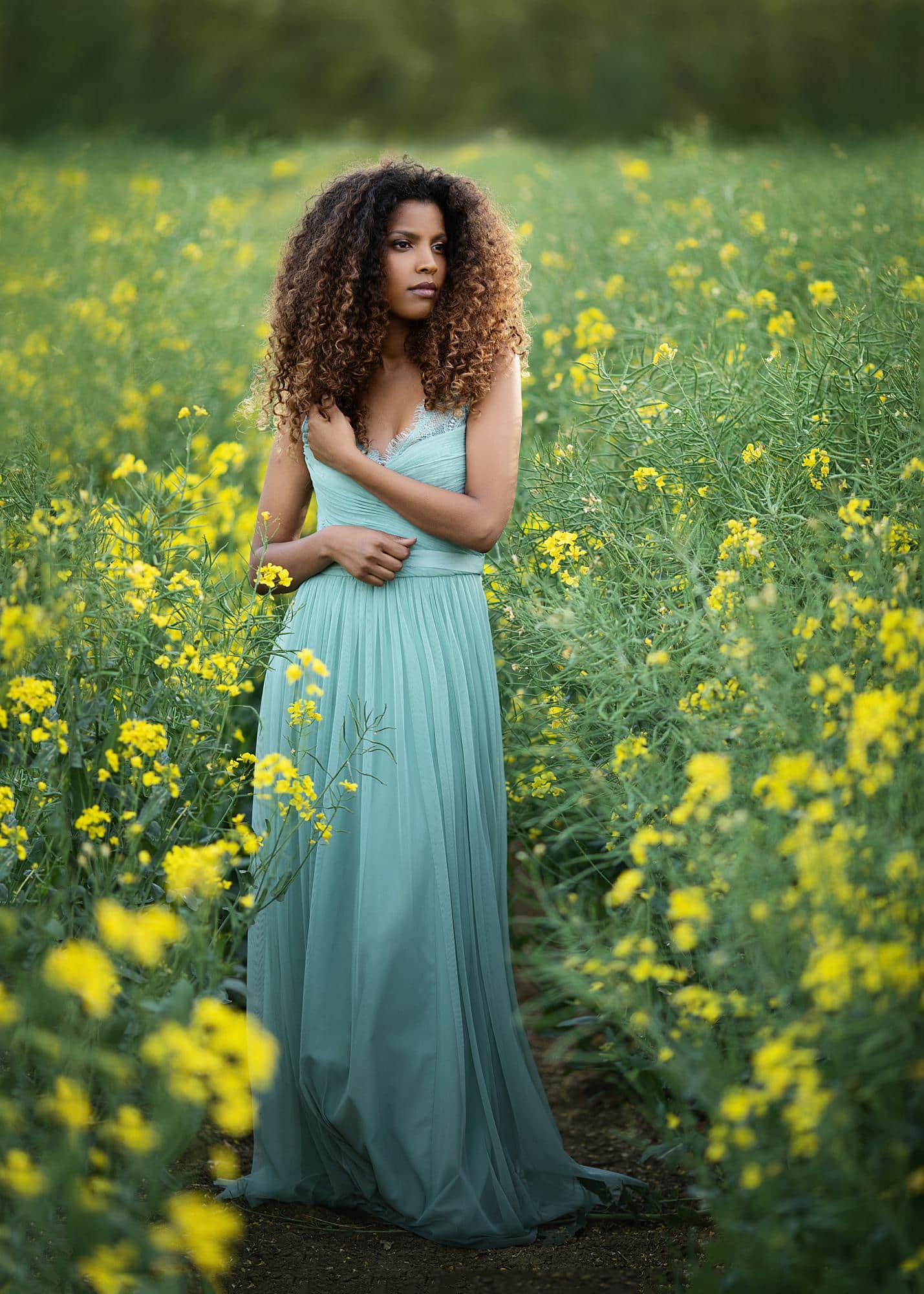 Brown haired woman in green dress poses for Beauty Shoot in a rape seed field Photoshoot in Suffolk