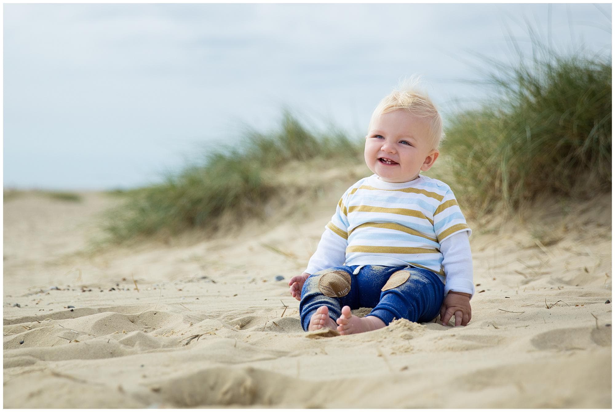 Baby boy sitting and smiling on Southwold Beach, in Suffolk