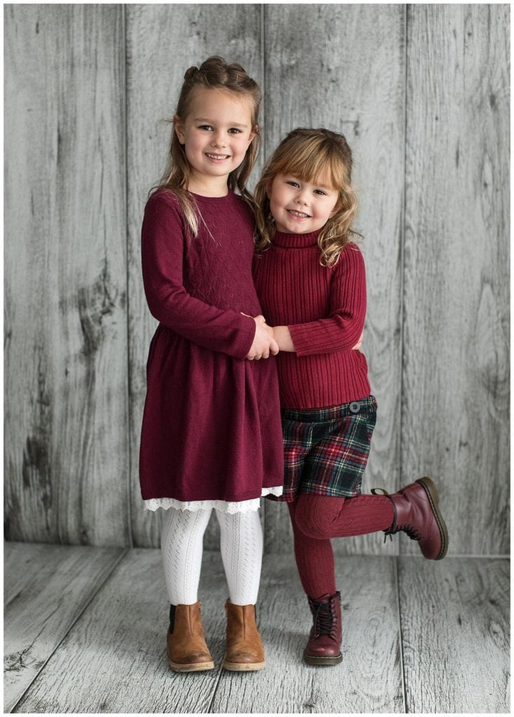 Two sisters wearing winter clothes pose for a Portrait Photoshoot on a grey wood background