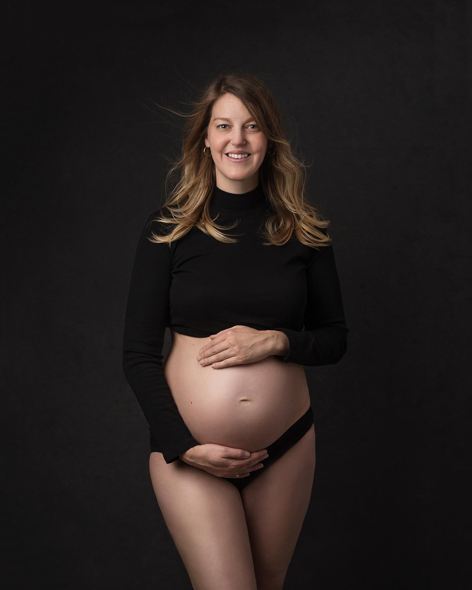 Pregnant woman posing in a black top and pants for a maternity photoshoot in Alison McKenny's Suffolk studio