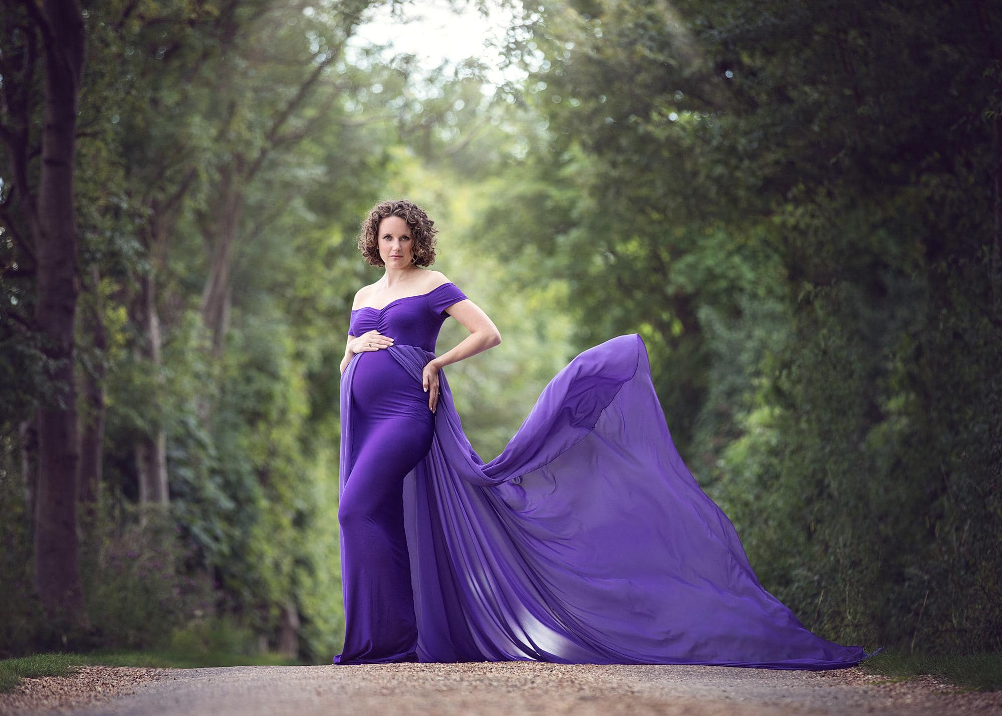 Pregnant woman posing in a purple dress for a maternity photoshoot on a country lane in Suffolk