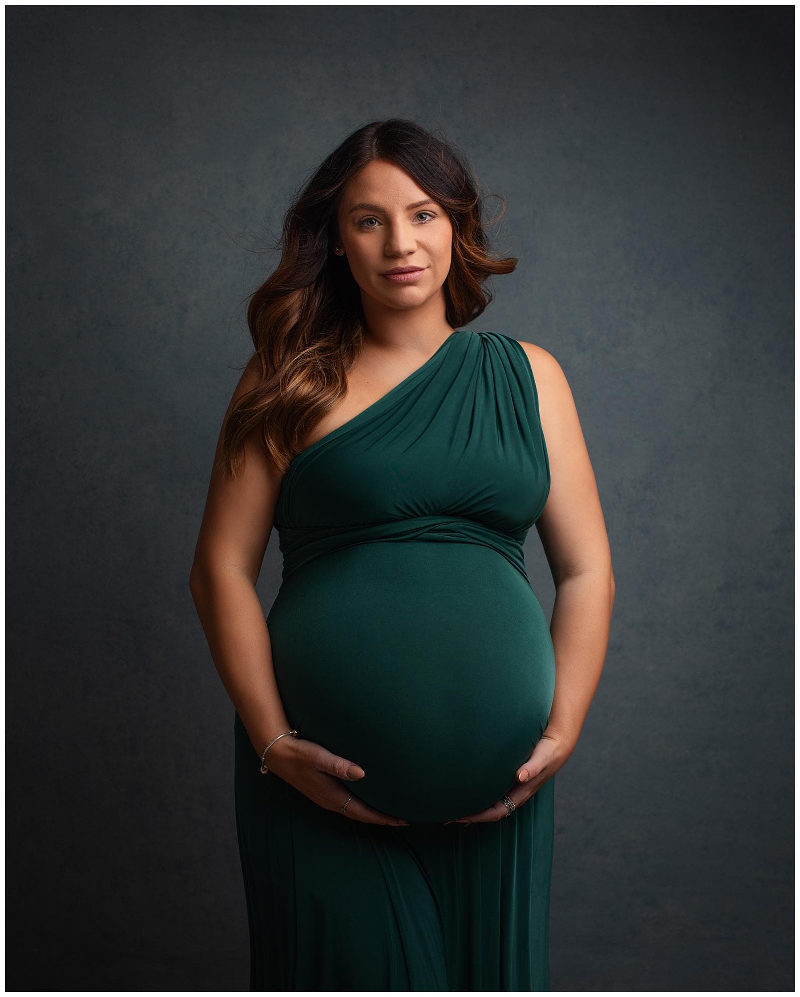 Pregnant woman posing in an emerald green dress for a maternity photoshoot in Alison McKenny's Suffolk studio
