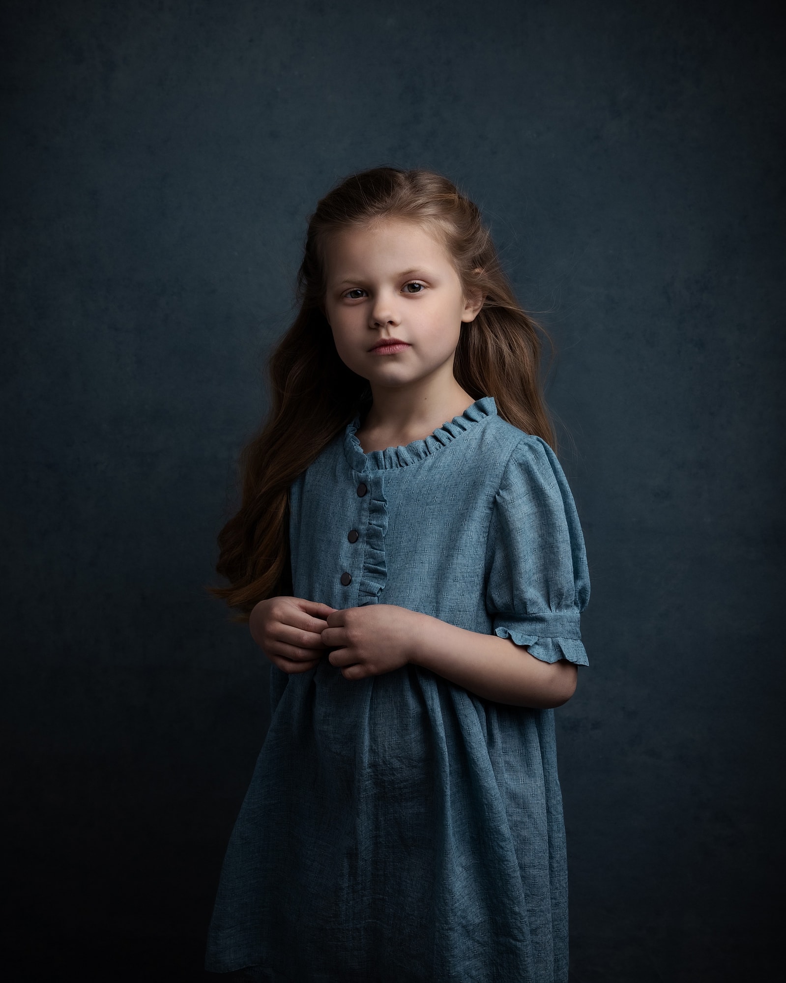 Little girl wearing a blue dress stands against a blue background during fine art photoshoot at Suffolk Studio