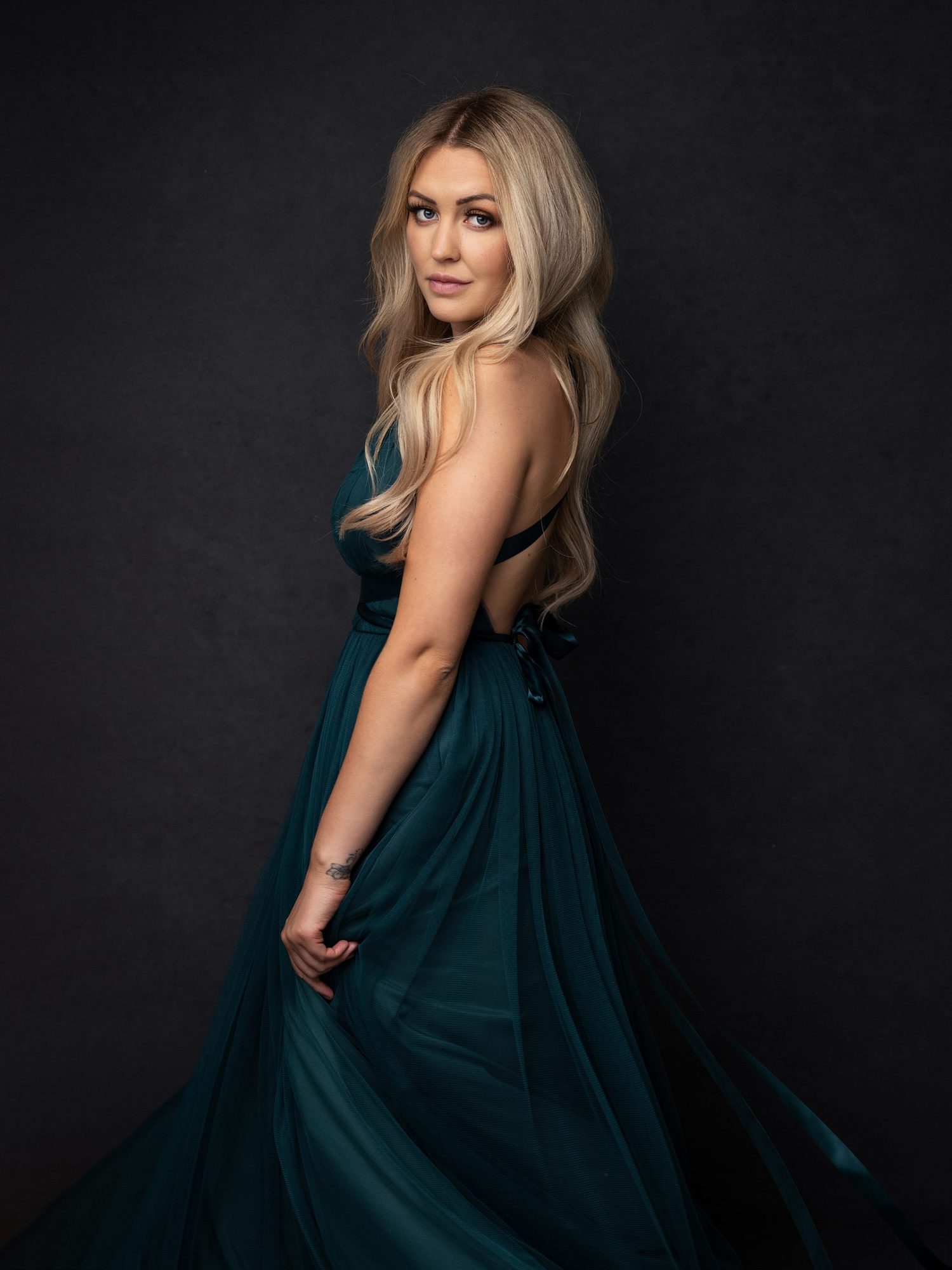 Blonde woman looks over her shoulder during her Beauty Photo shoot while wearing a green dress