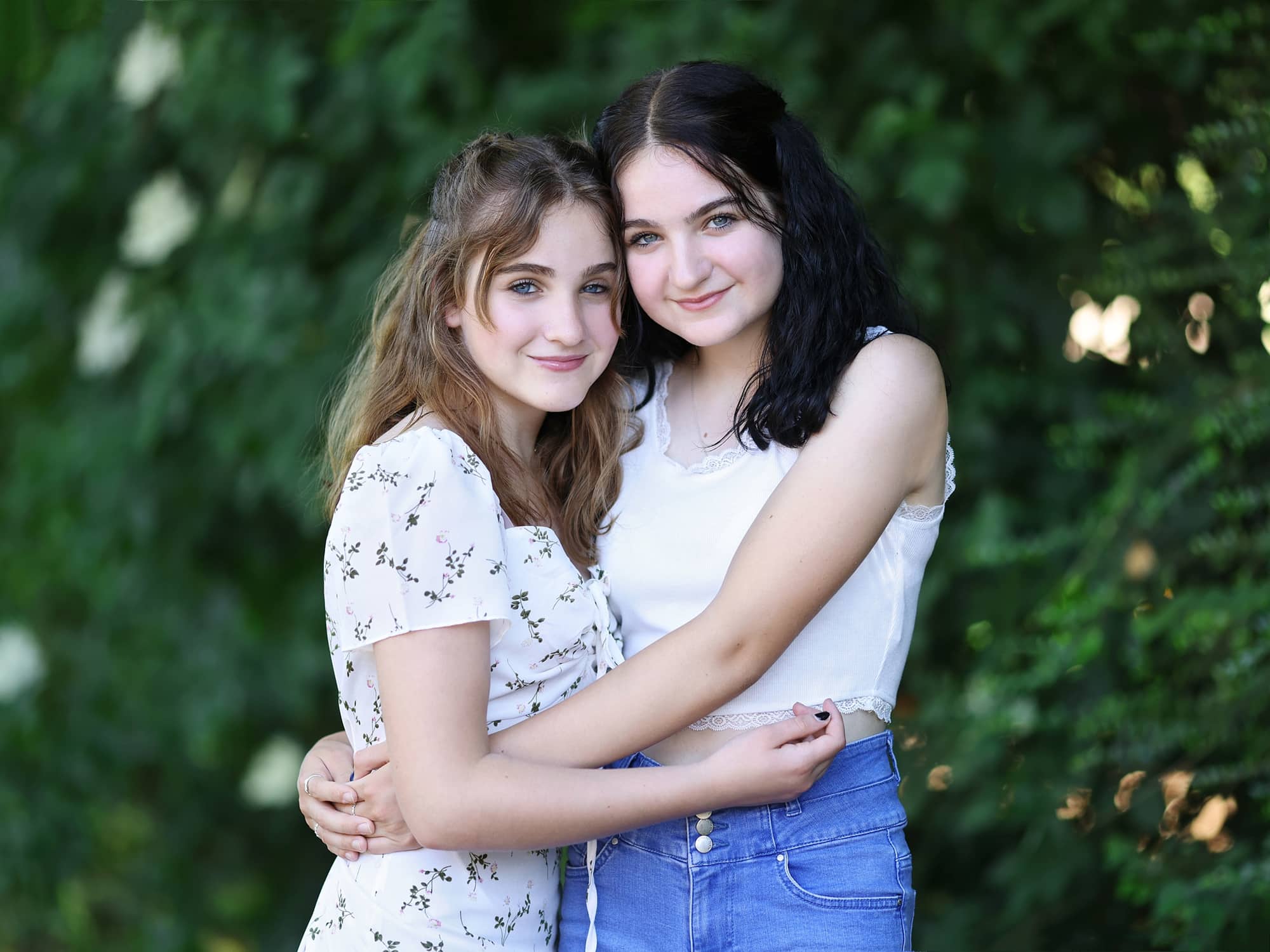 Two Sisters smile as they hug each other against a green background during family photoshoot in Suffolk