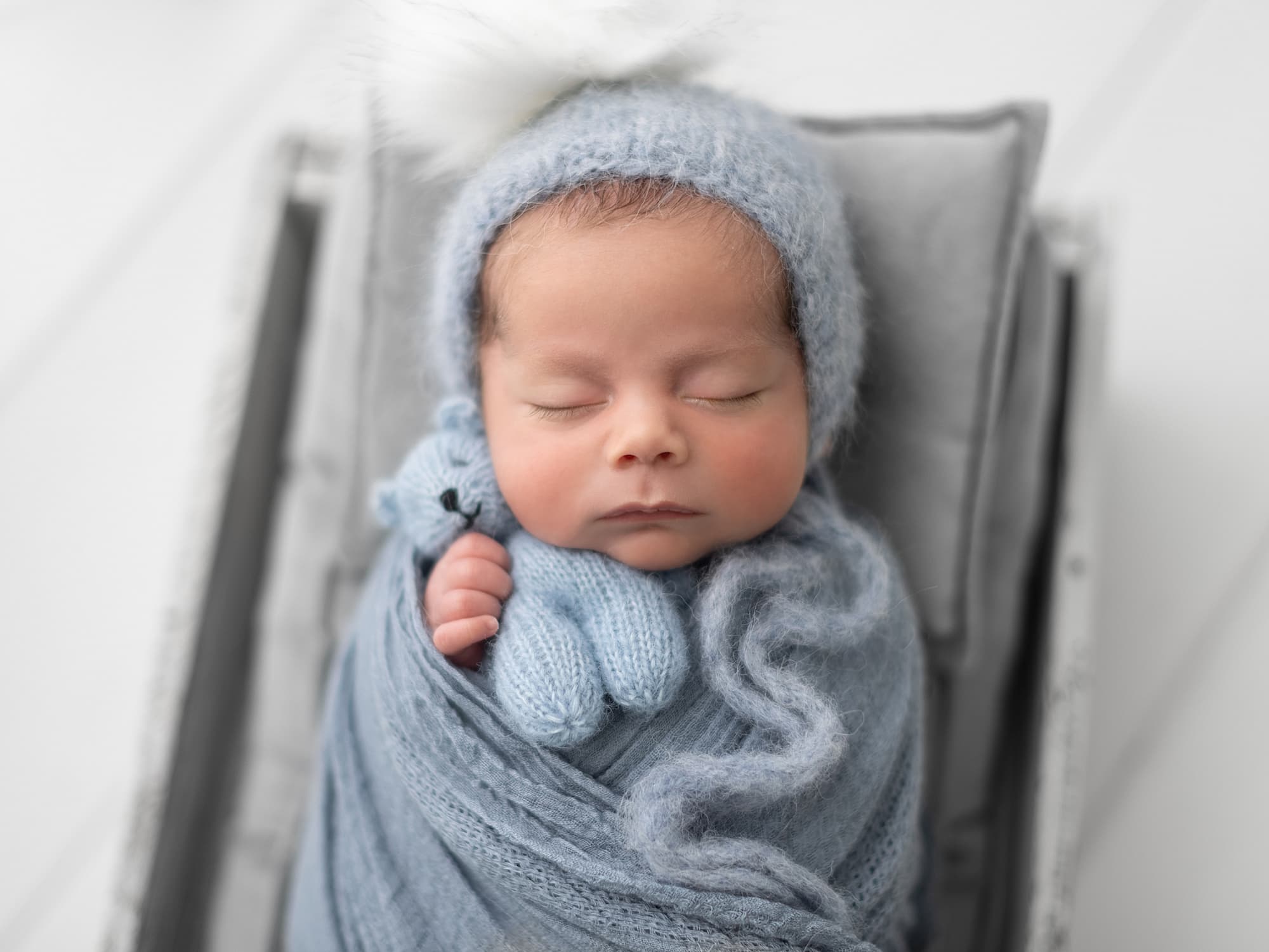 Baby boy in white wooden crate cuddles his blue teddy during his Newborn Photoshoot in Suffolk Studio