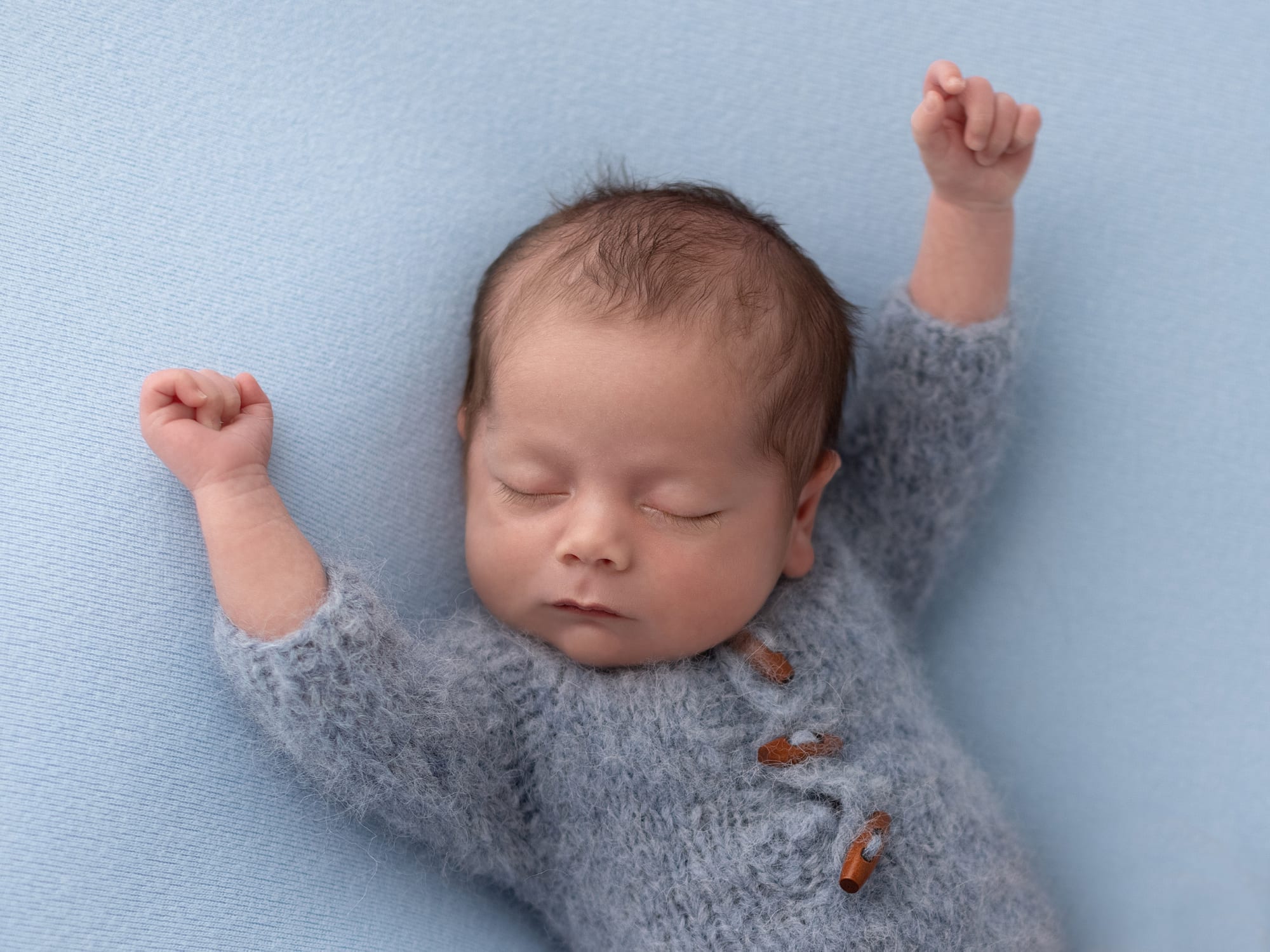 Baby boy in blue wool romper stretches during his Newborn Photoshoot in Suffolk Studio