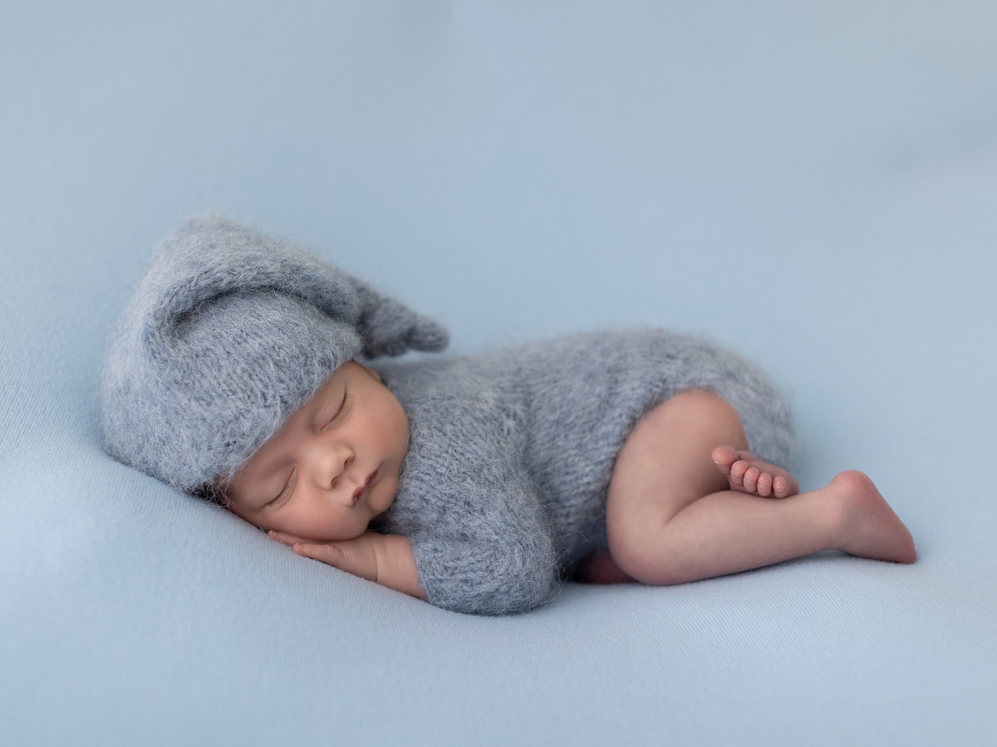 Baby boy in blue wool romper and sleepy hat lying on his front during his Newborn Photoshoot in Suffolk Studio