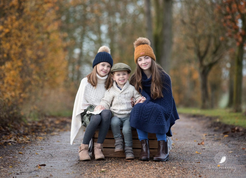 Autumnal photo of 3 siblings in warm jumpers and hats on Suffolk farm