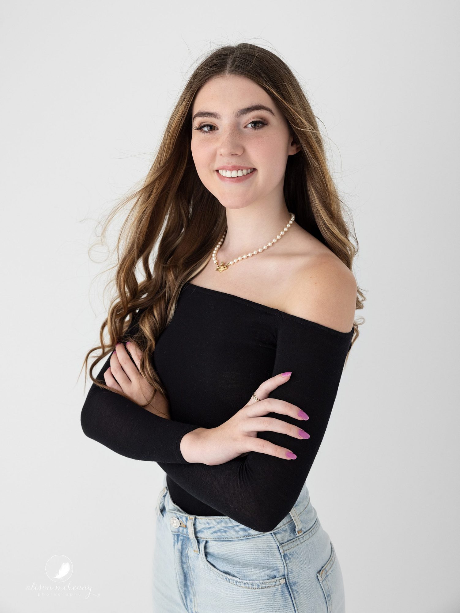 Long haired teen smiles with folded arms on white background