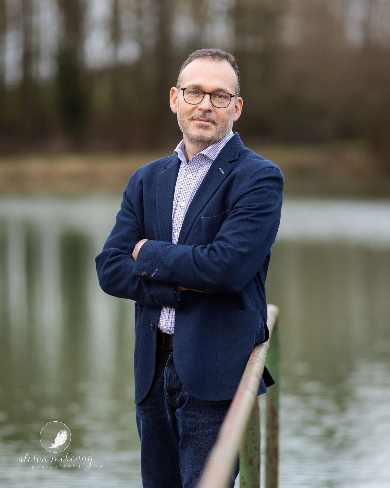 Man in a suit jacket and jeans standing next to a lake in a rural setting during a Personal Branding Photoshoot in Suffolk