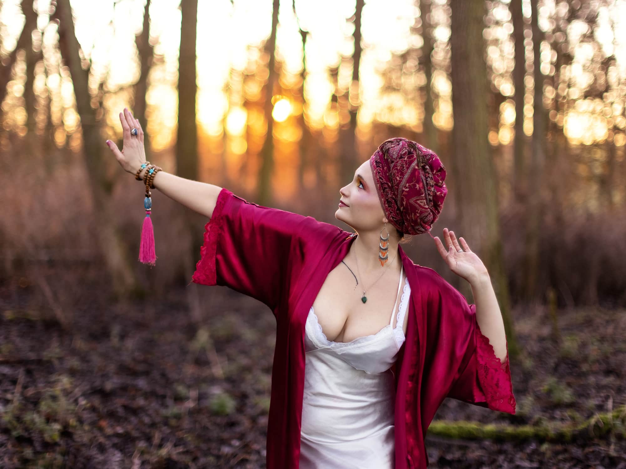 Priestess in a white satin nightdress and head scarf dances in the woods as the sun goes down