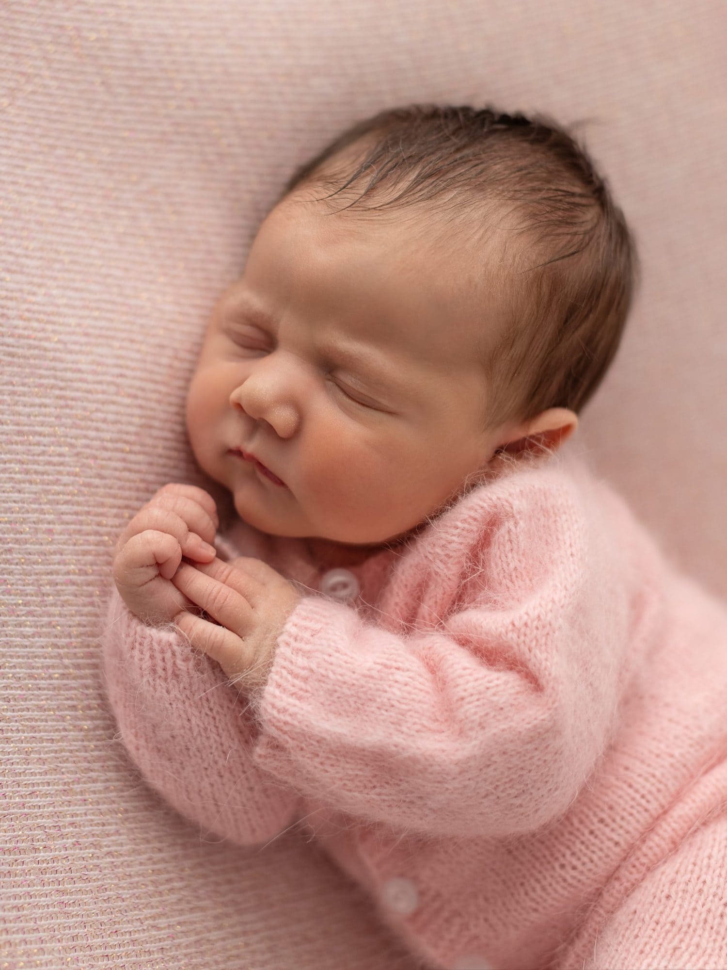 Newborn Baby Girl wearing a pink wool romper on a pink blanket