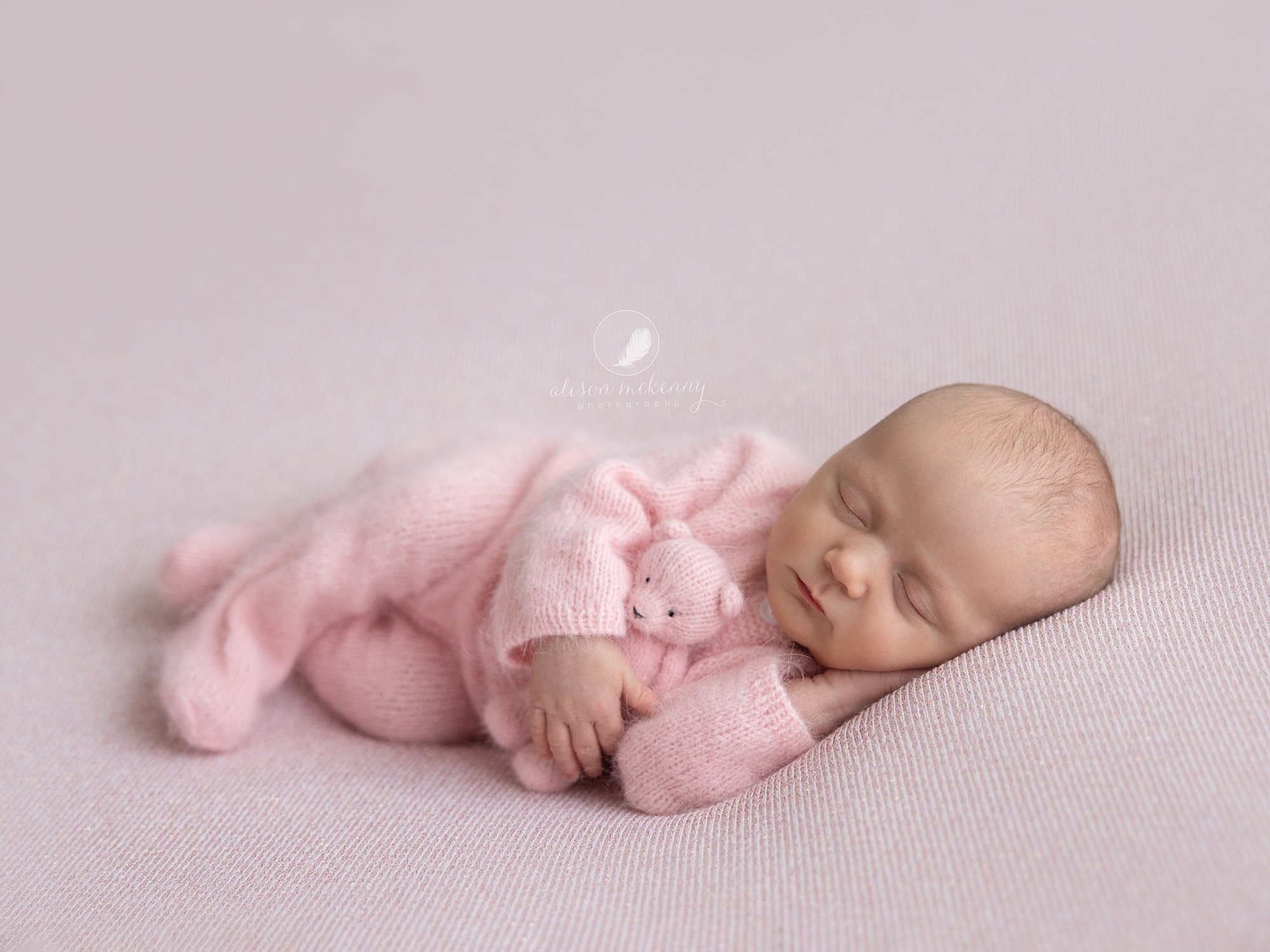 Newborn Baby Girl wearing a pink wool romper on a pink blanket with a pink teddy