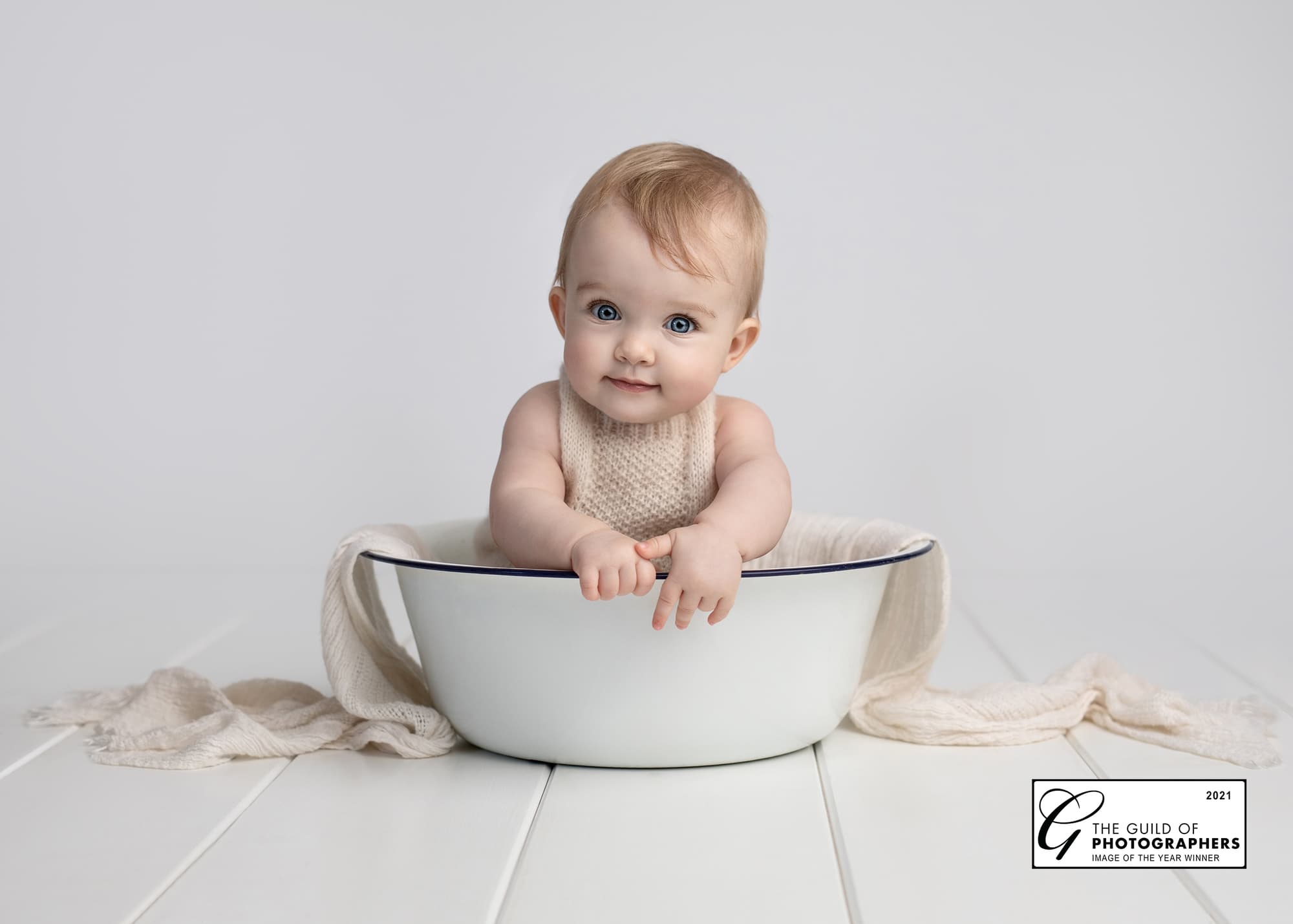 Baby Girl in a white tin bowl smiles at the camera on a white background.