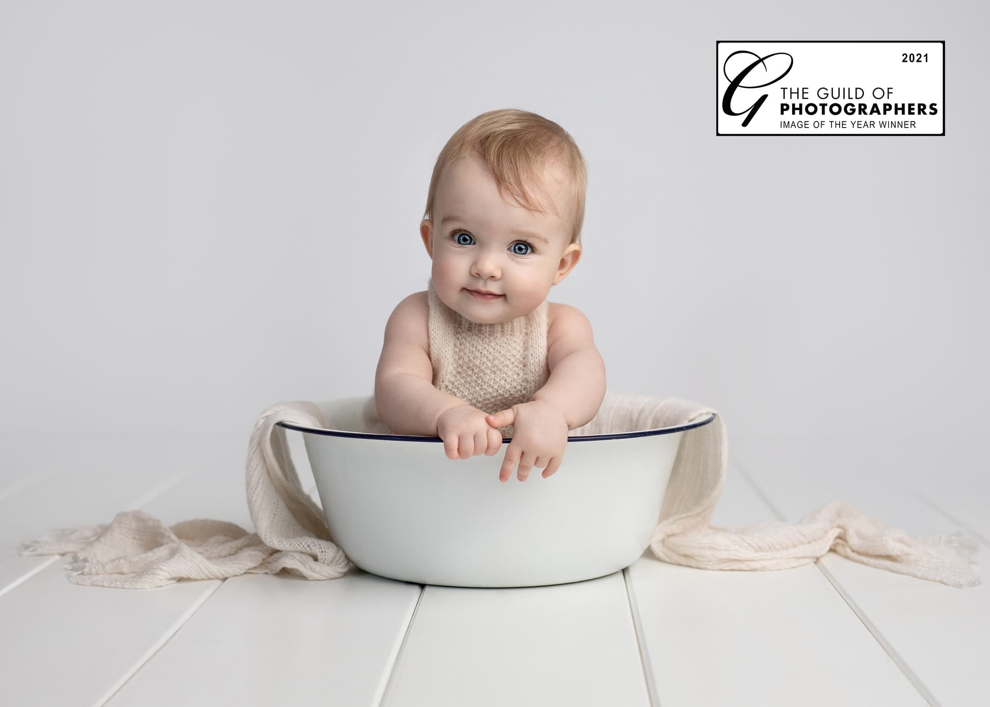 Baby Girl in a white tin bowl smiles at the camera on a white background.