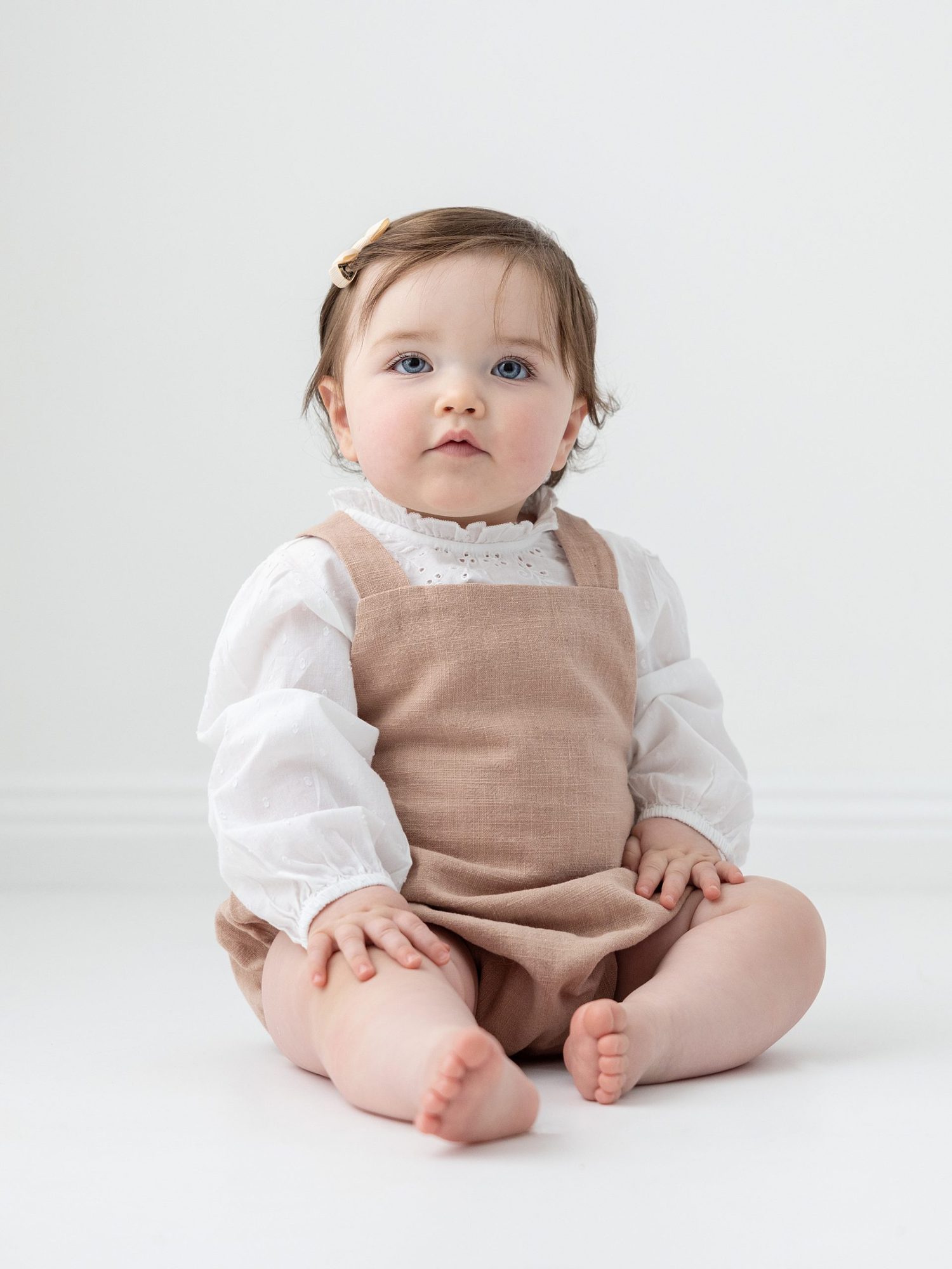 Beautiful Baby Girl sitting in a smart white blouse and beige linen romper