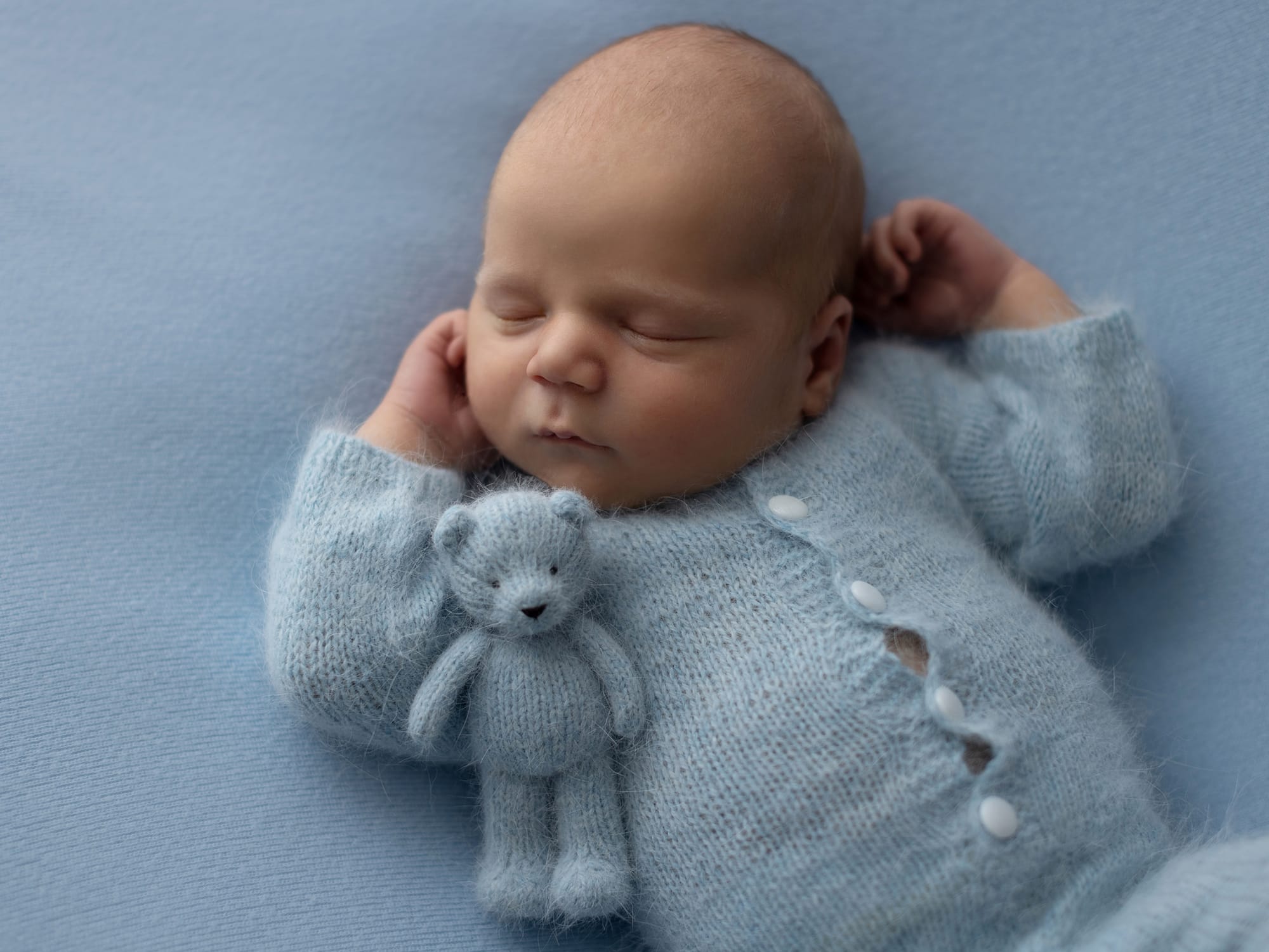 Newborn Baby Boy in a blue wool romper sleeping with his blue wool Teddy