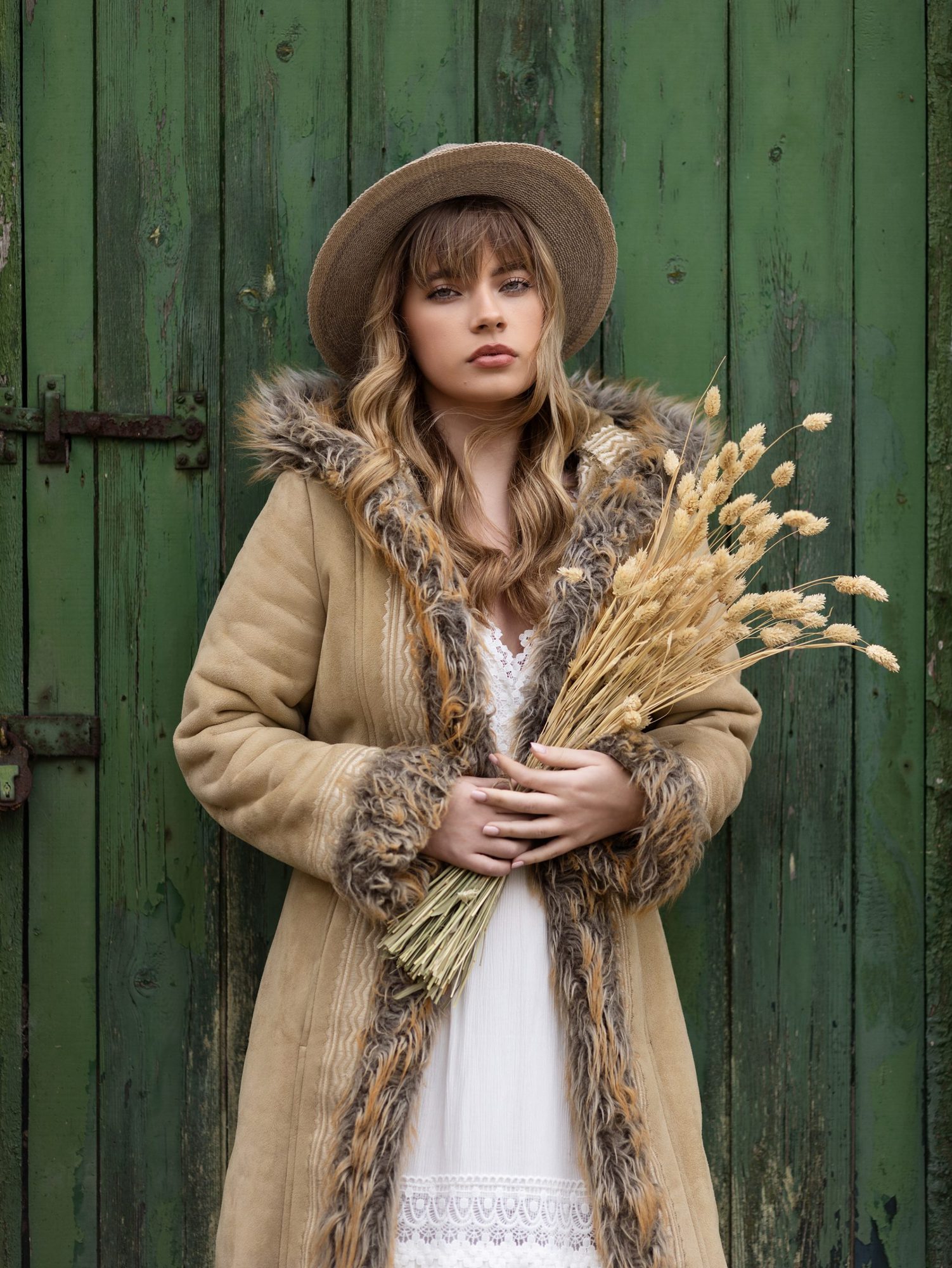 Teenage girl in a white dress neck and a sheepskin coat holds some dried flowers