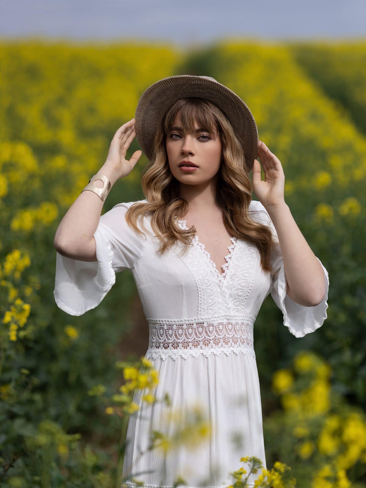 Teenage girl in a white dress stands with her face to the sun in a Rape Seed Field