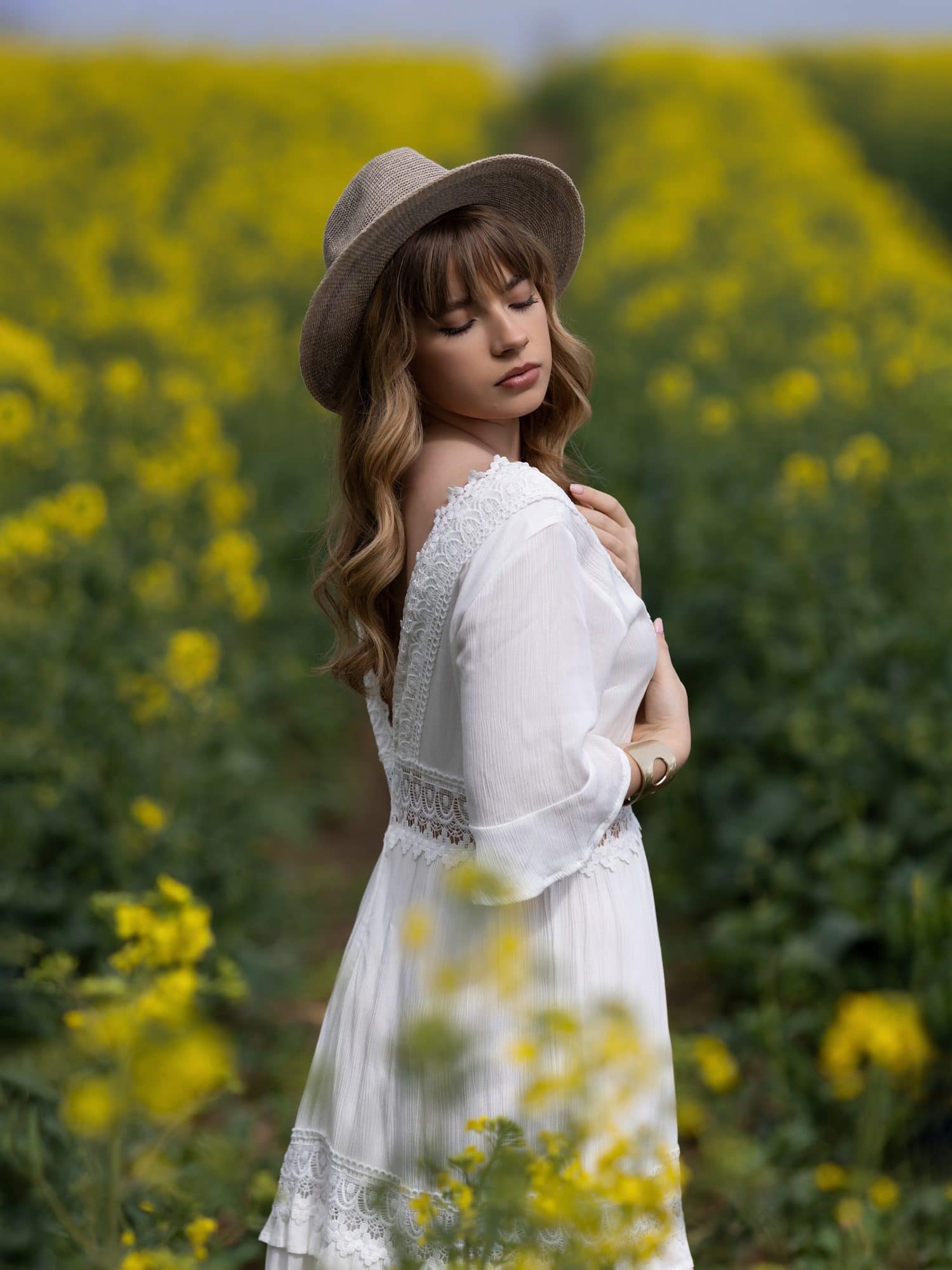 Teenage girl in a white dress stands with her face to the sun in a Rape Seed Field