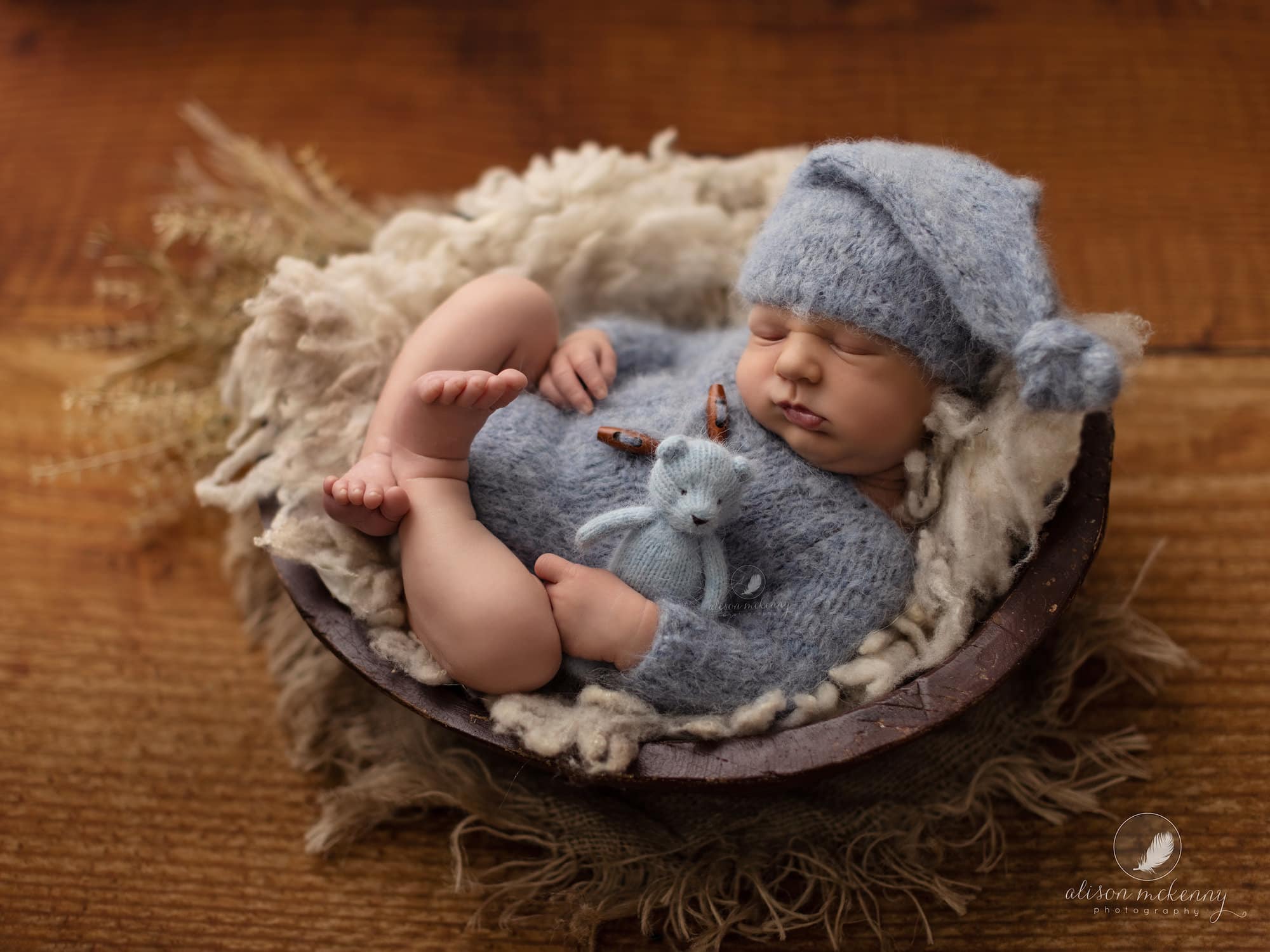 Newborn baby boy lies in a wooden bowl during Newborn Photoshoot at Suffolk Photography Studio