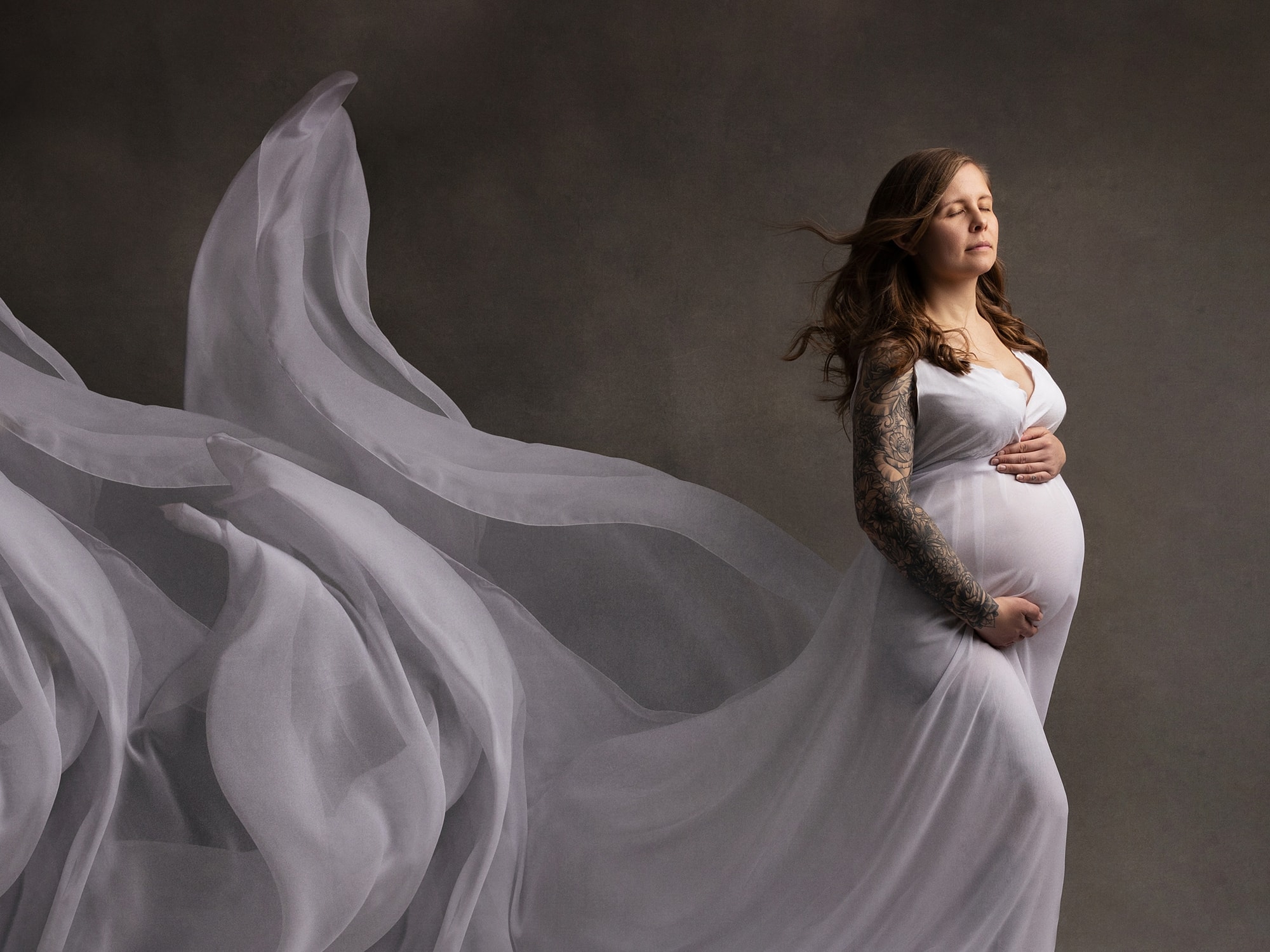Portrait of Pregnant woman holding her belly with a white dress blowing behind her