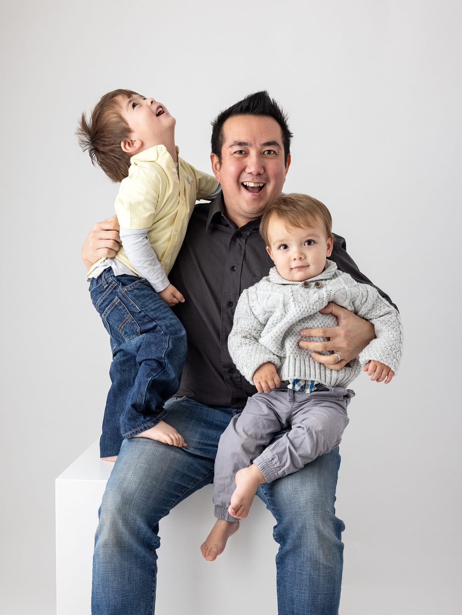 Two little boys and their Dad laughing during a studio family photoshoot with a white background