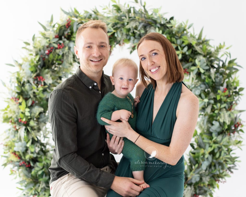 Family wearing green pose in front of a Christmas Wreath in Suffolk studio