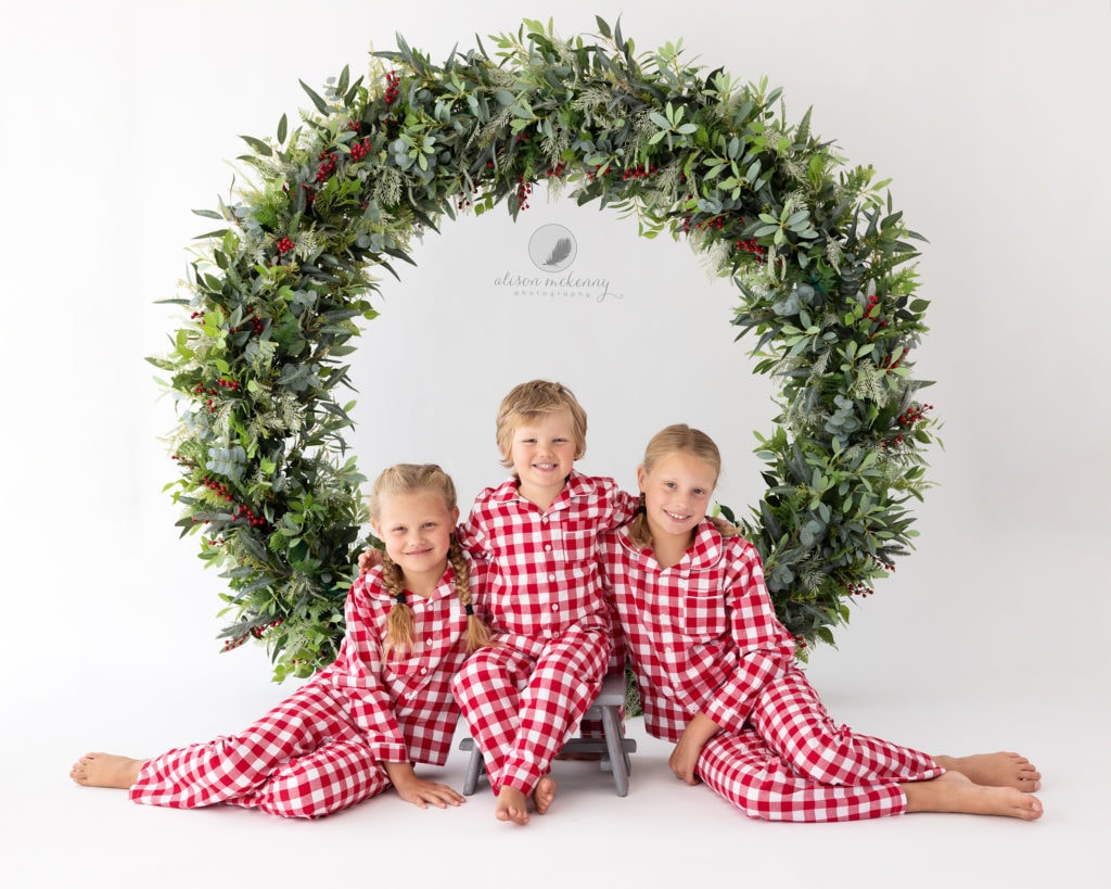 3 Siblings wearing red and white pyjamas sat on floor during Christmas Mini Session in Suffolk Studio
