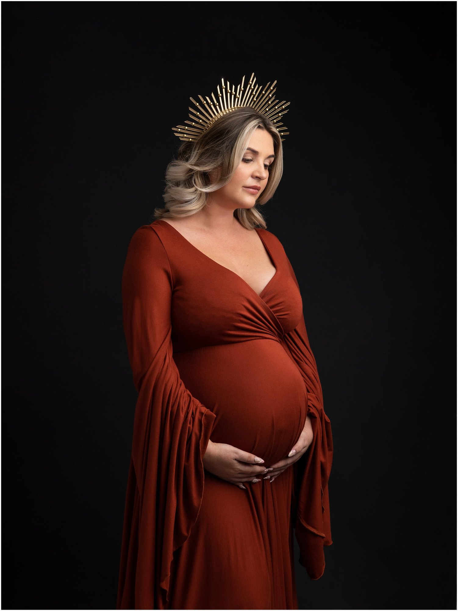 Pregnant lady in rust orange dress and crown poses during maternity photoshoot with Suffolk Photographer Alison McKenny