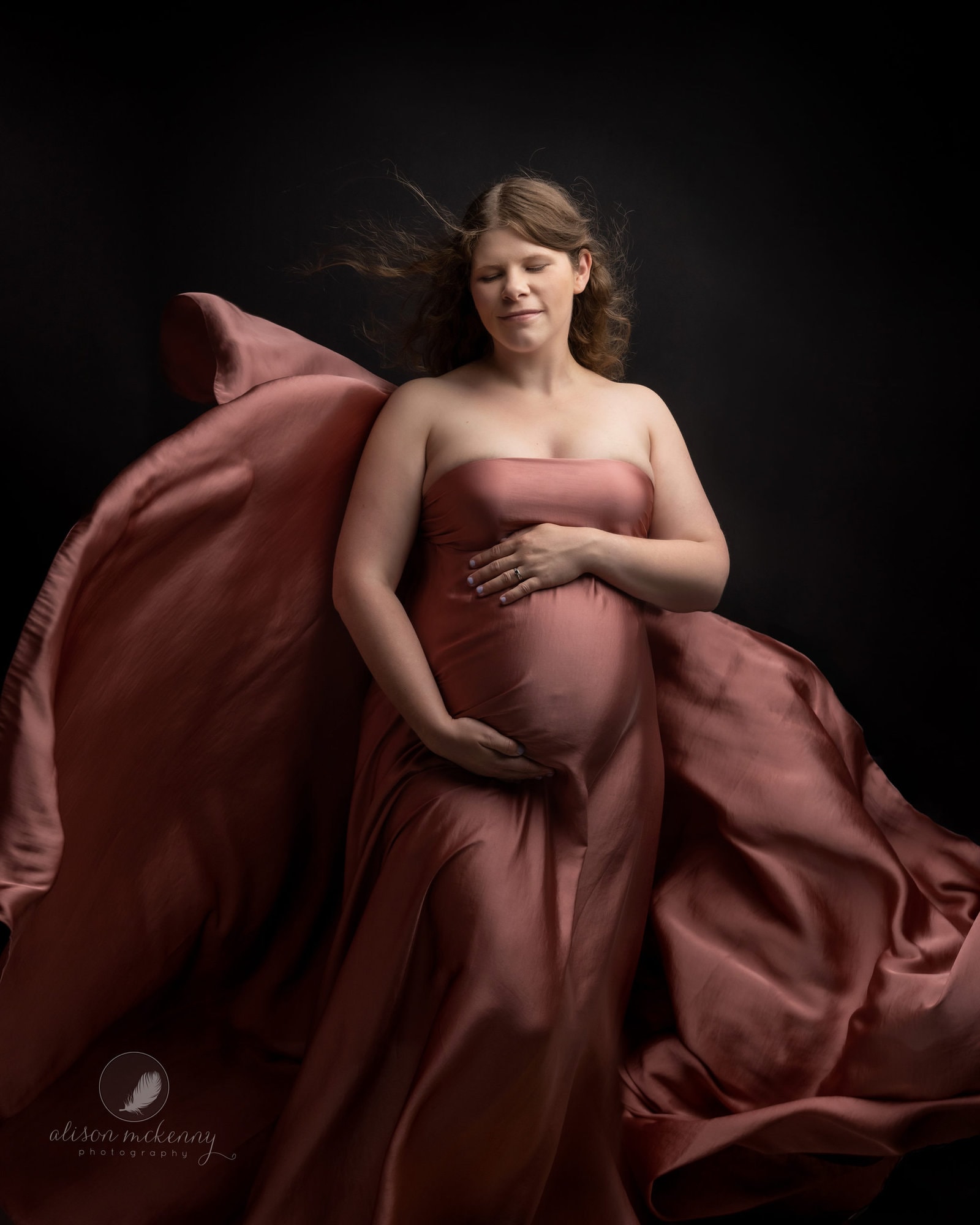 Pregnant lady in silk material poses during maternity photoshoot with Suffolk Photographer Alison McKenny