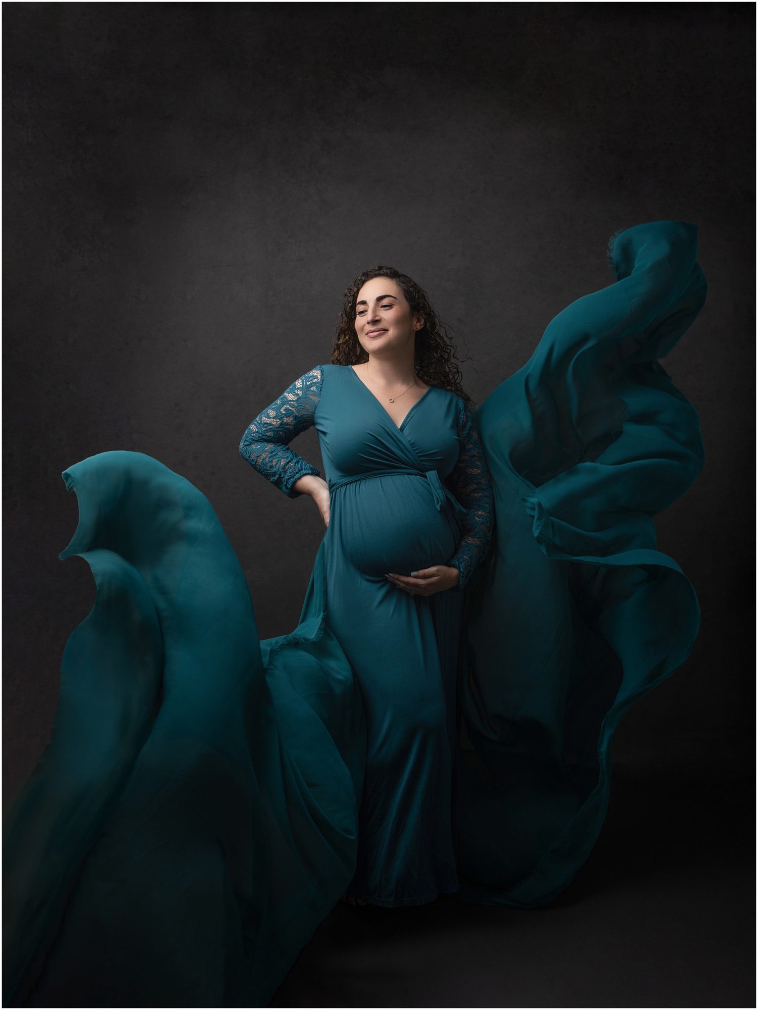 Pregnant lady in Teal Dress poses while holding her bump during photoshoot with Alison McKenny