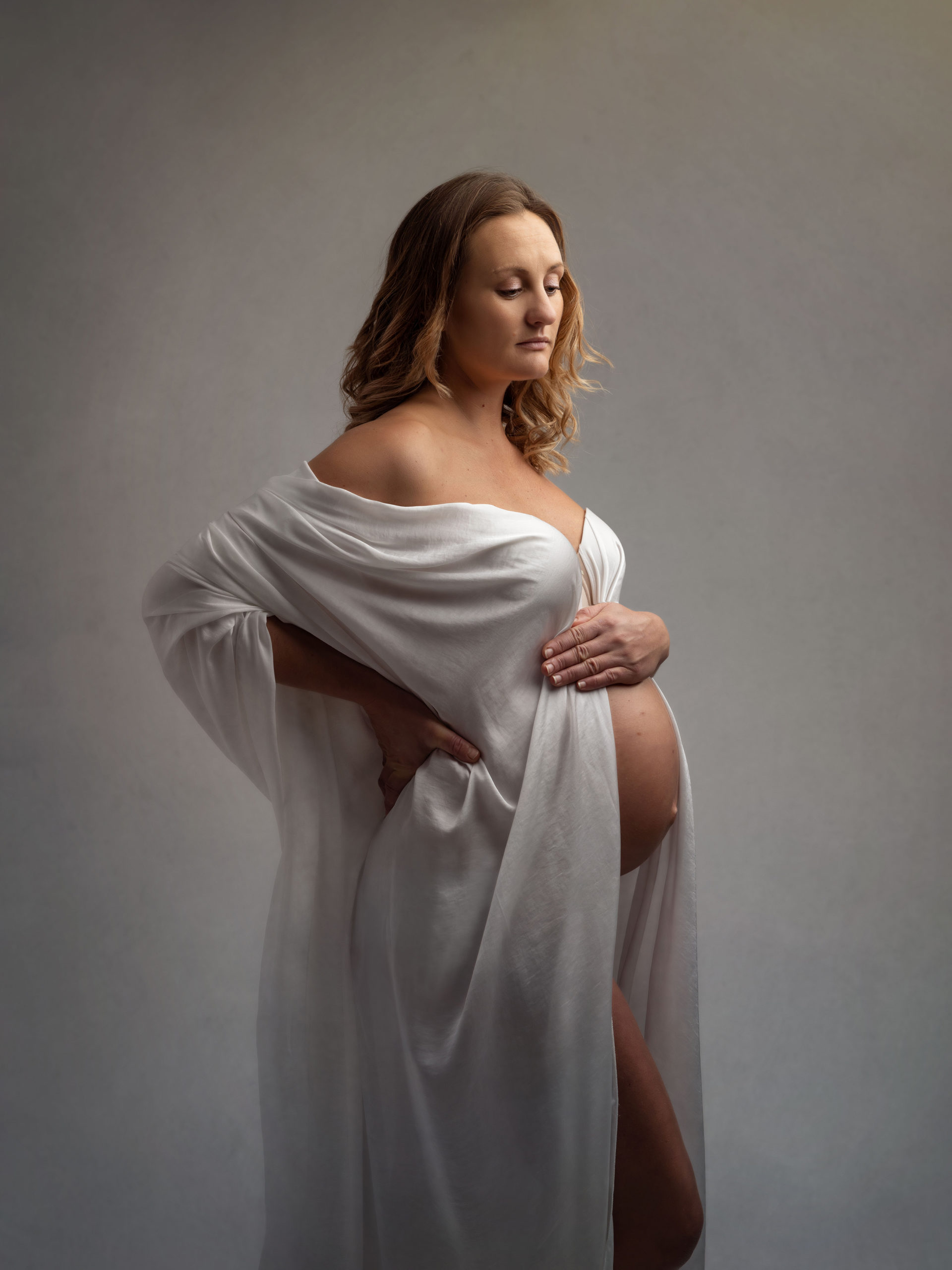 Pregnant woman draped in white material poses for Maternity Shoot with Alison McKenny Photography