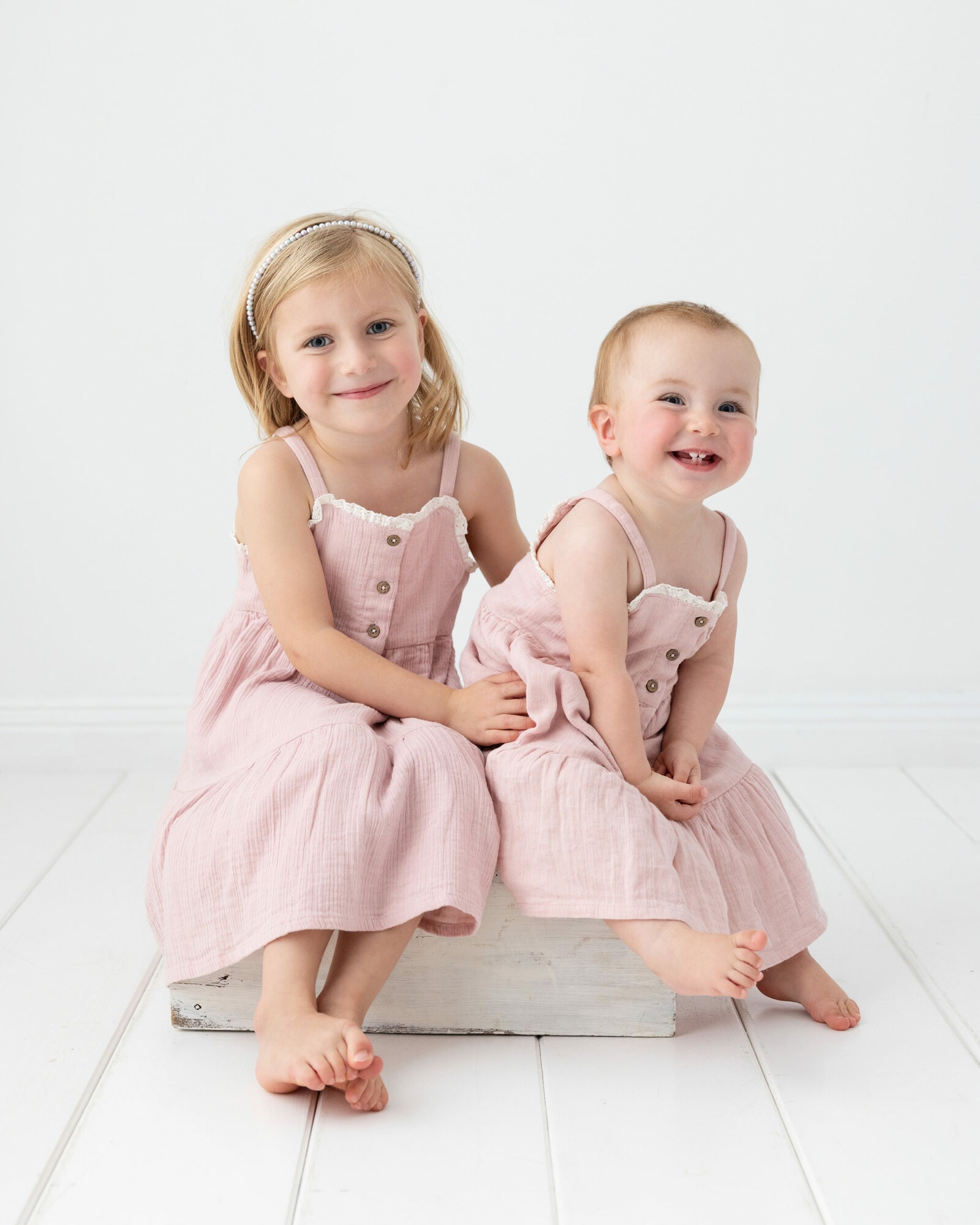 Young sisters dressed in matching pink dresses on white background