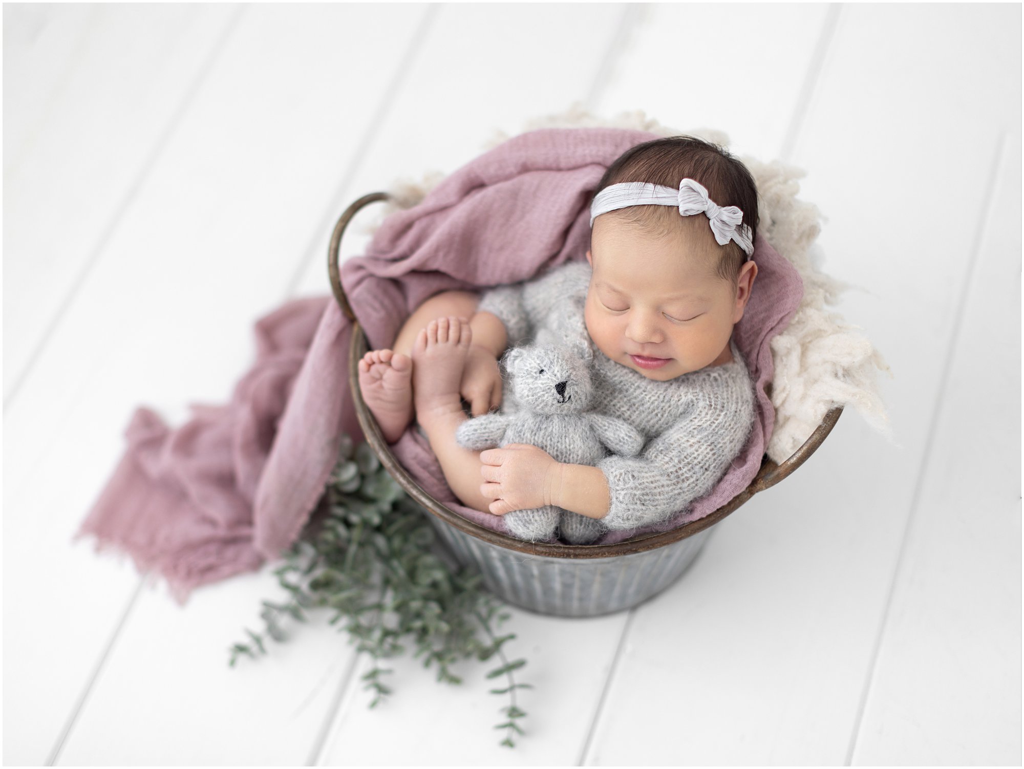 Newborn Baby Girl sits in a bucket and smiles during her photoshoot with Alison McKenny Photography