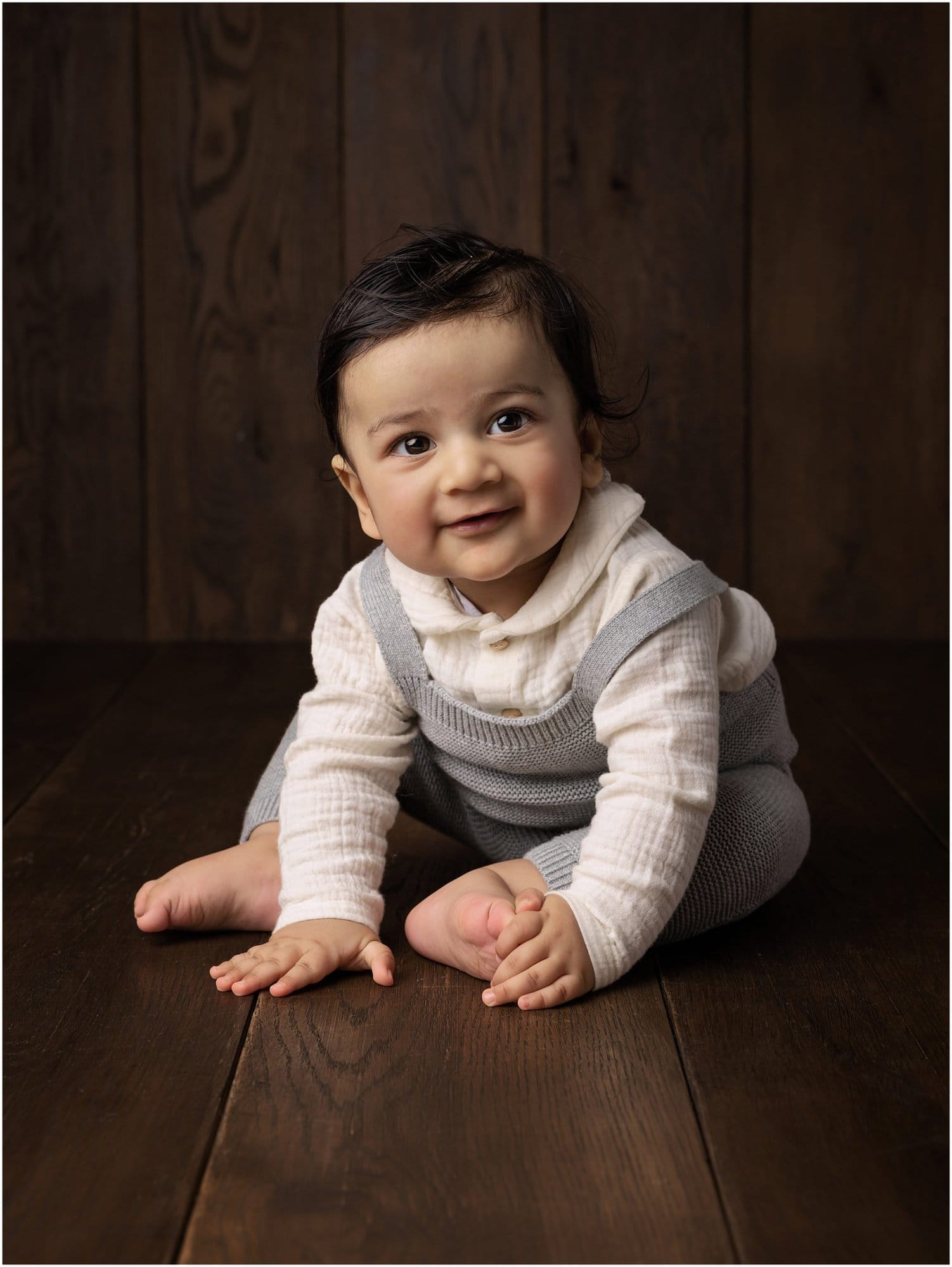 Baby sitting up on dark wood floor and smiles during his Baby Photoshoot with Alison McKenny Photography