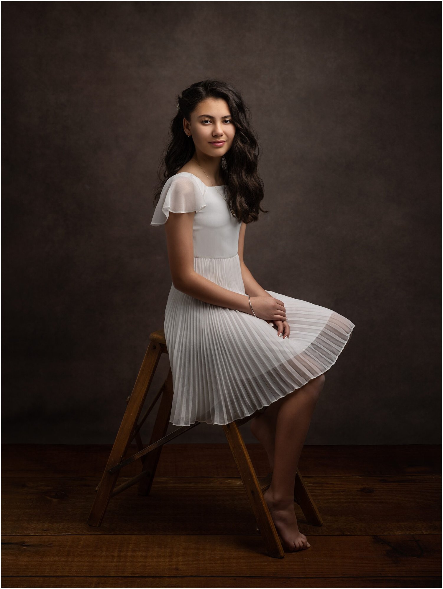 Pre teen girl in a white dress sits on a stool during a Fine Art Photoshoot with Alison McKenny Photography